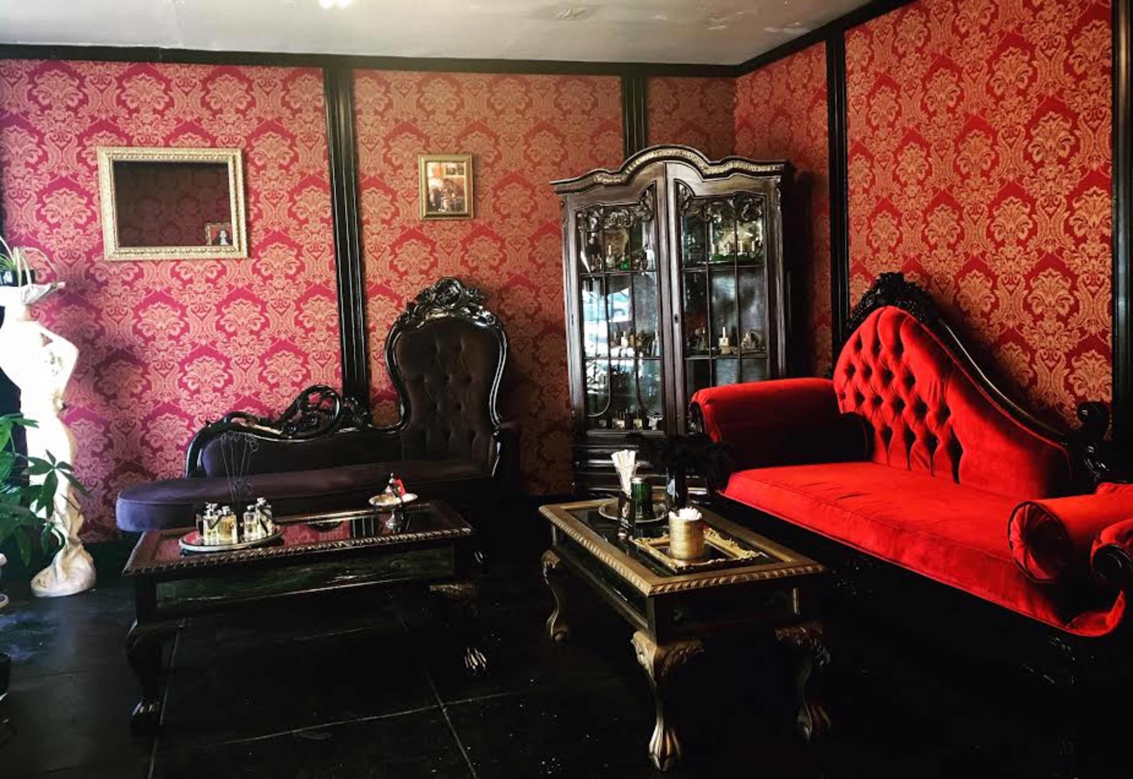 The image shows a room with red-patterned walls, featuring two ornate sofas—one black and one red—alongside a glass cabinet and a coffee table.