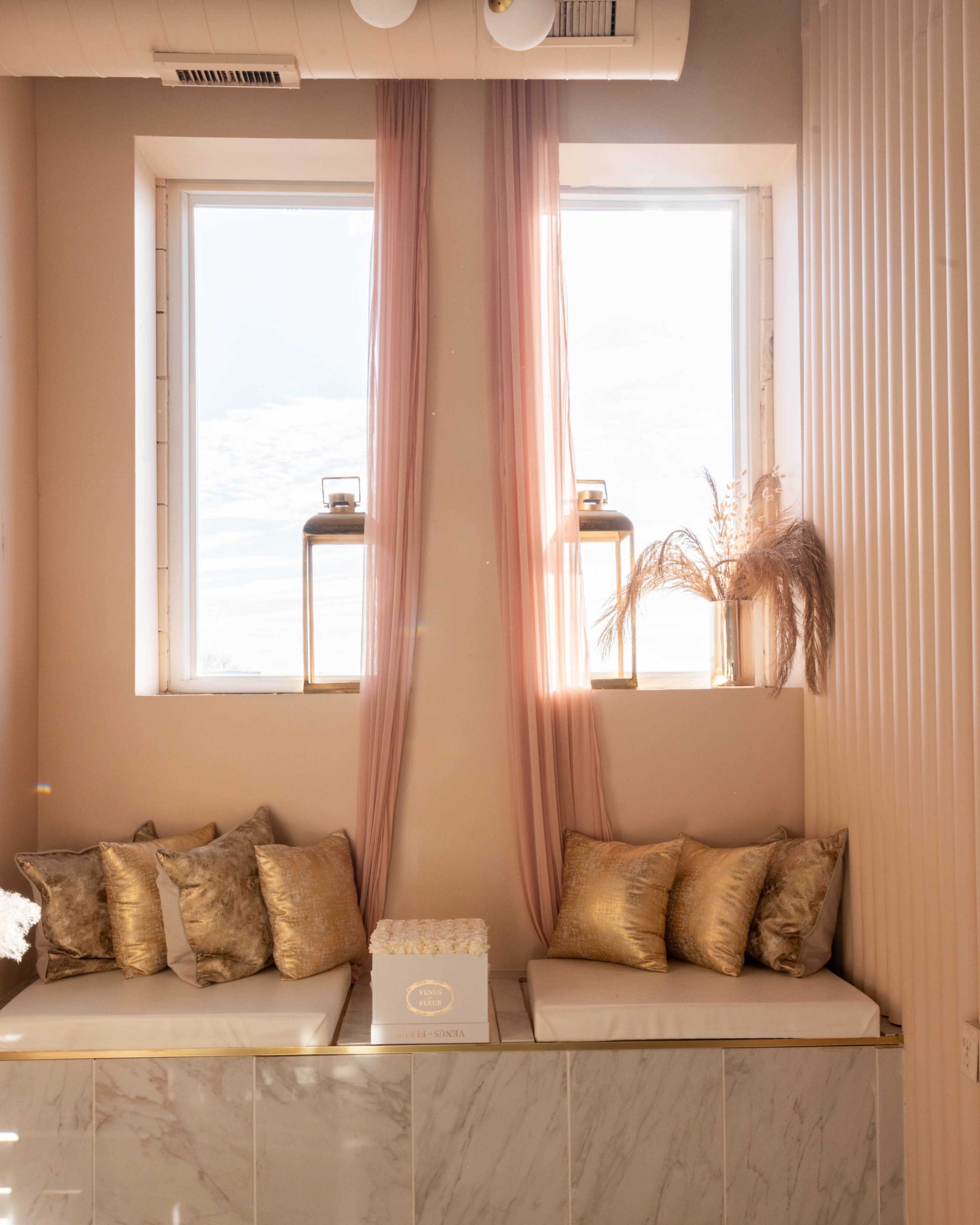 A cozy nook features a window with sheer curtains, illuminated by natural light, complemented by plush cushions and decorative lanterns.