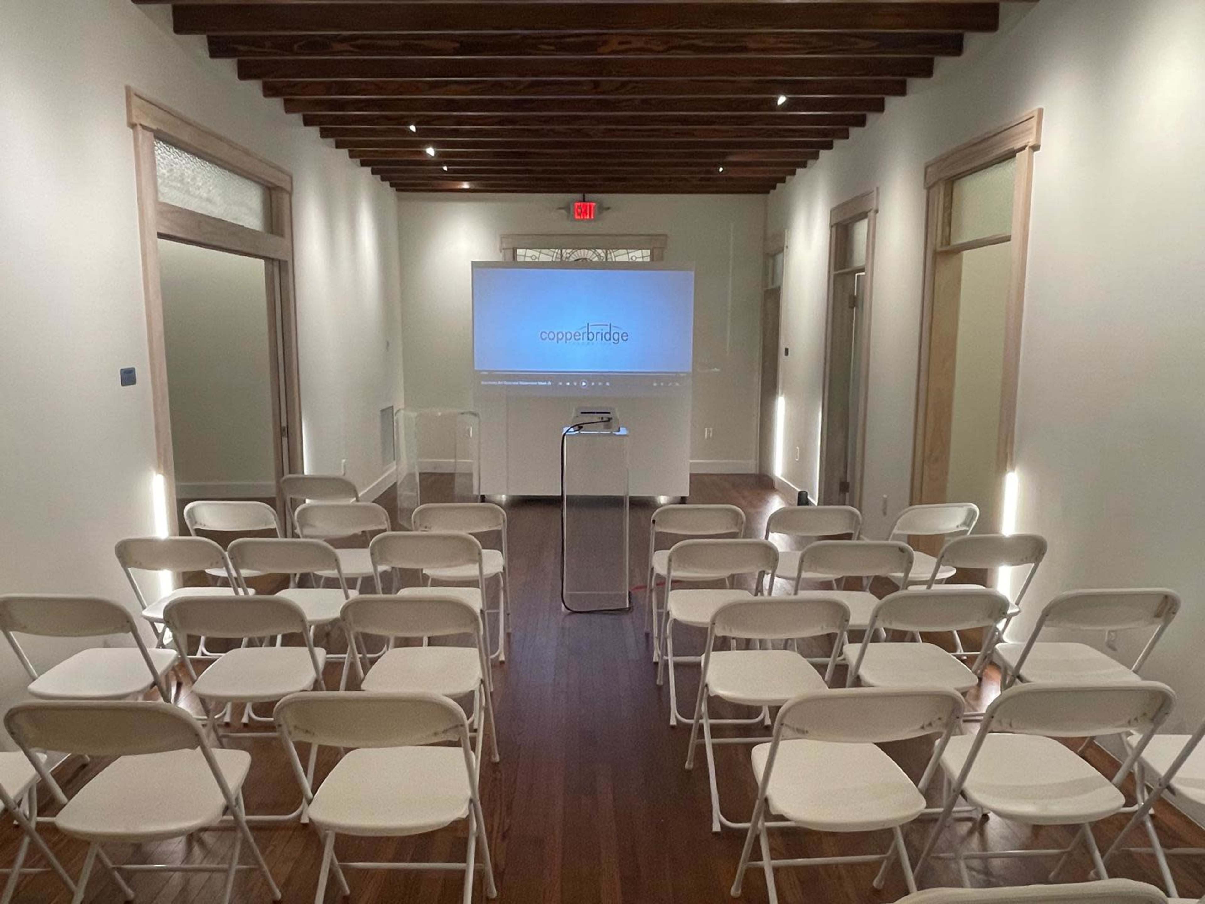 A conference room filled with white chairs facing a projection screen displaying the word "cooperbridge."