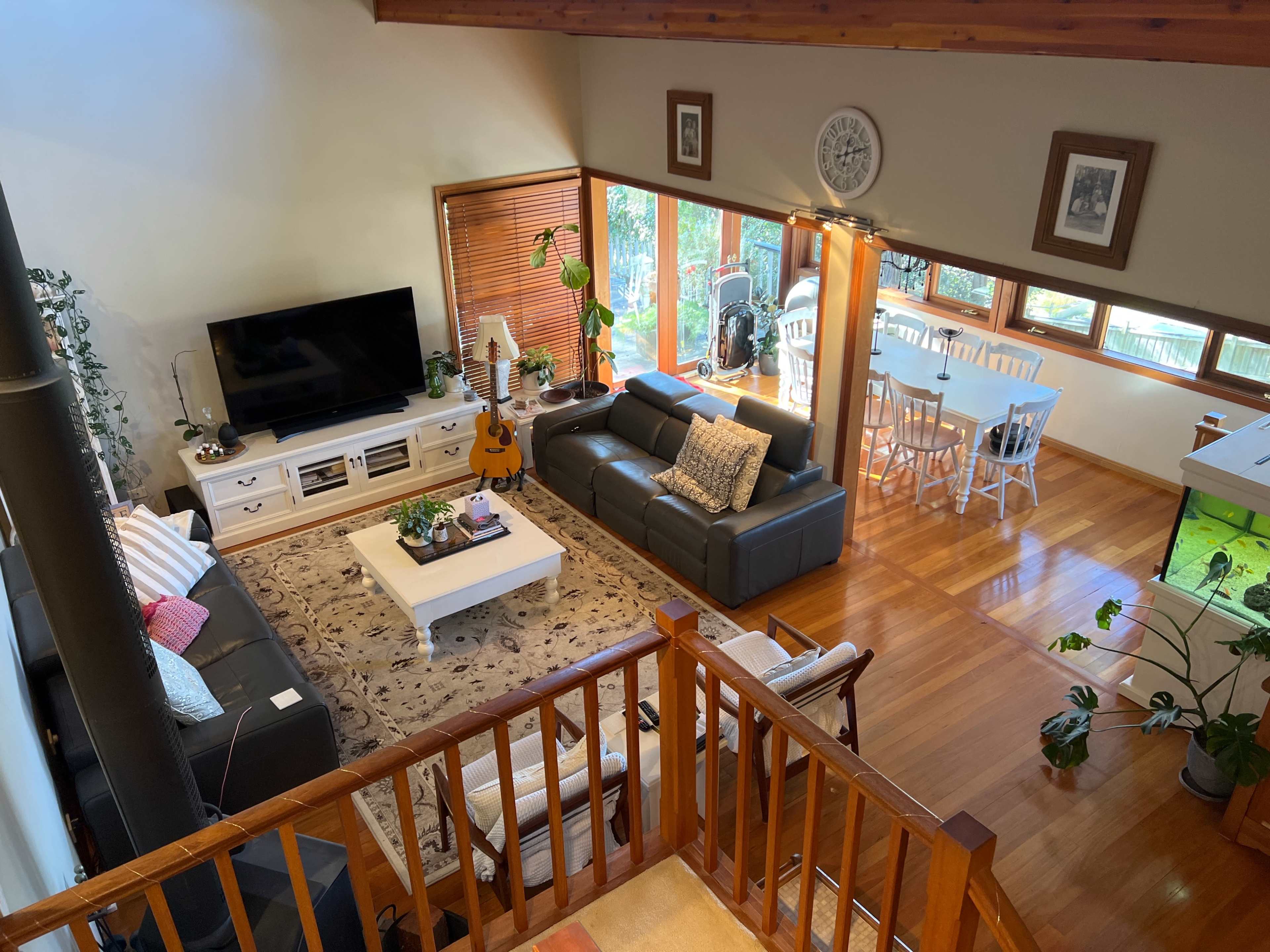 A spacious living area with a TV, a guitar, and a dining table surrounded by large windows that let in natural light.