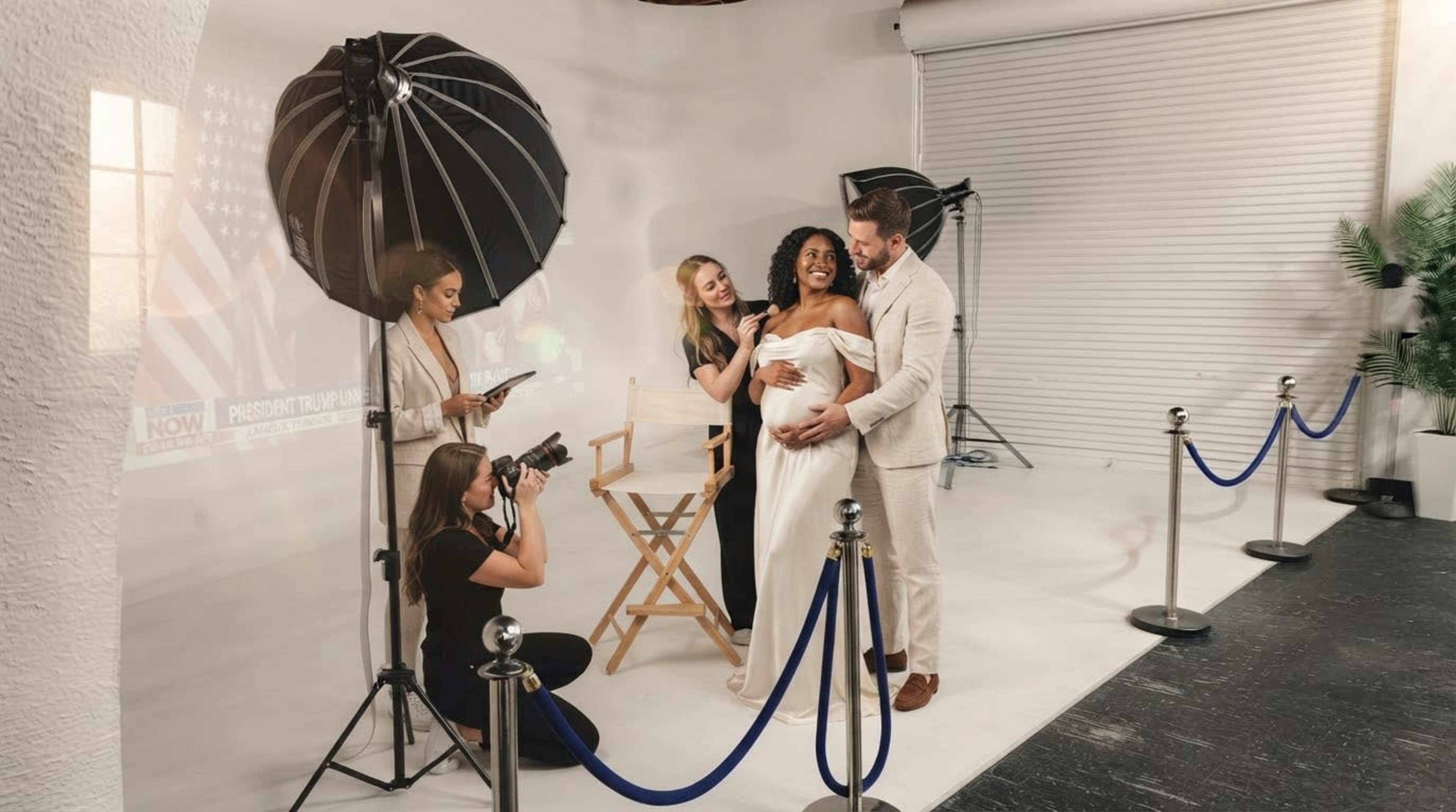 A bride in a white dress poses with a groom while a photographer captures the moment, and two stylists make final adjustments.
