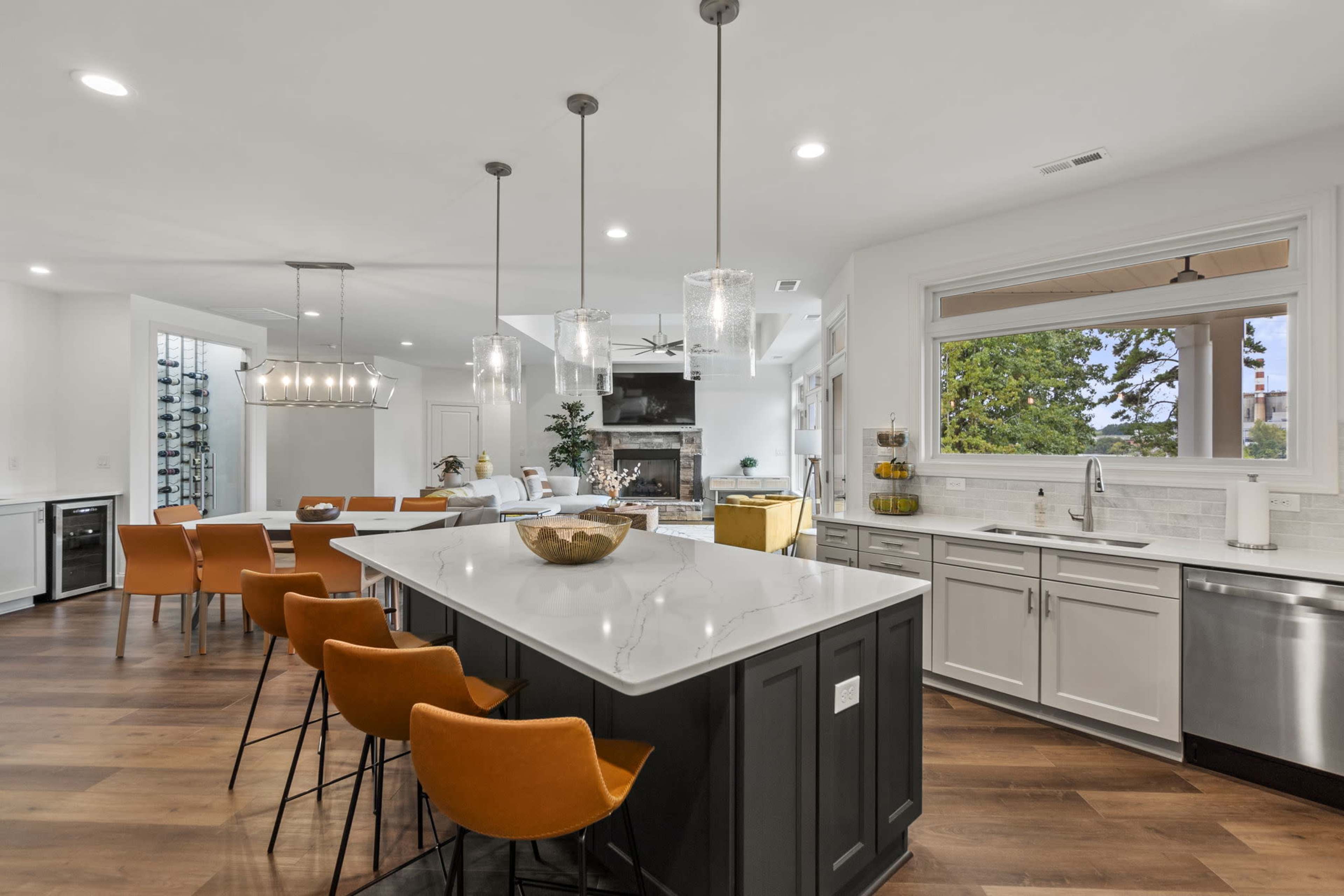 A modern kitchen features a large island with seating, pendant lights, and a dining area, all set against a backdrop of wooden flooring and white cabinetry.