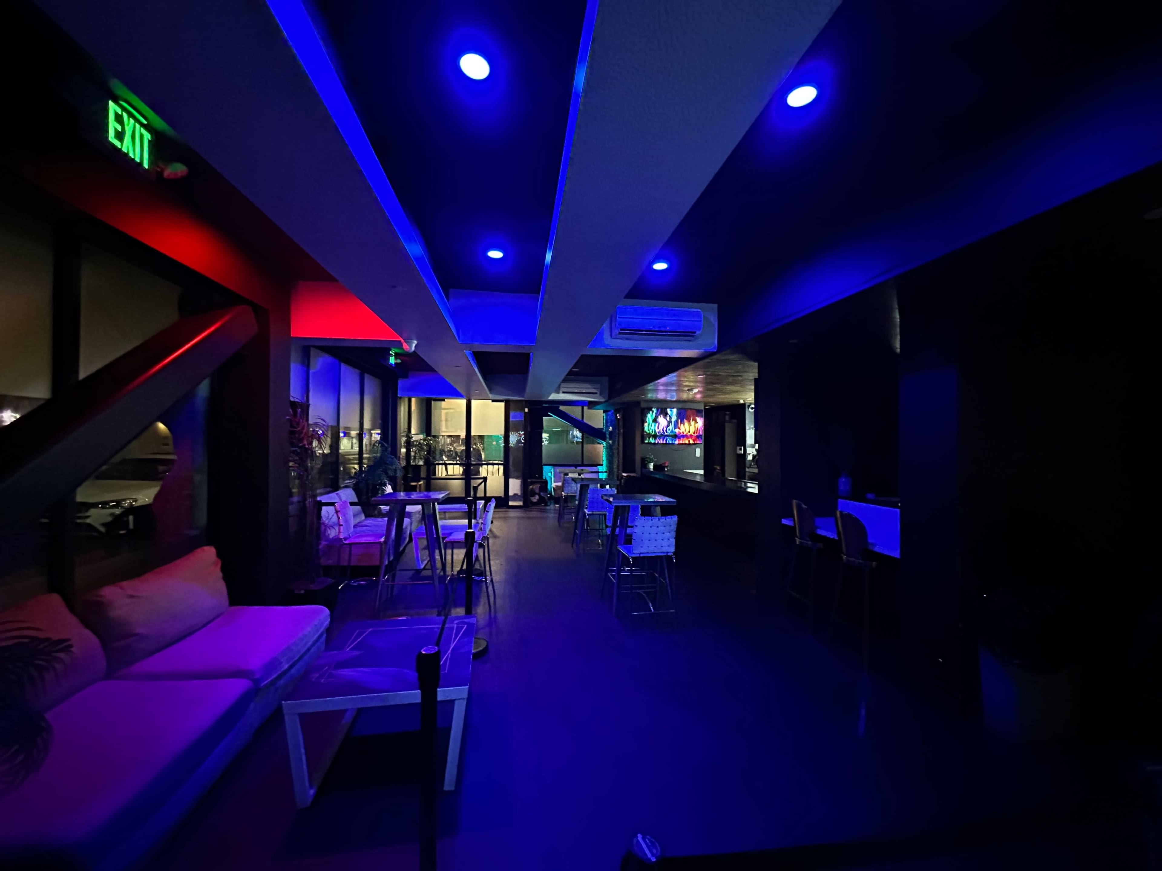 A dimly lit lounge features blue and red lighting, with seating areas and a bar visible in the background.