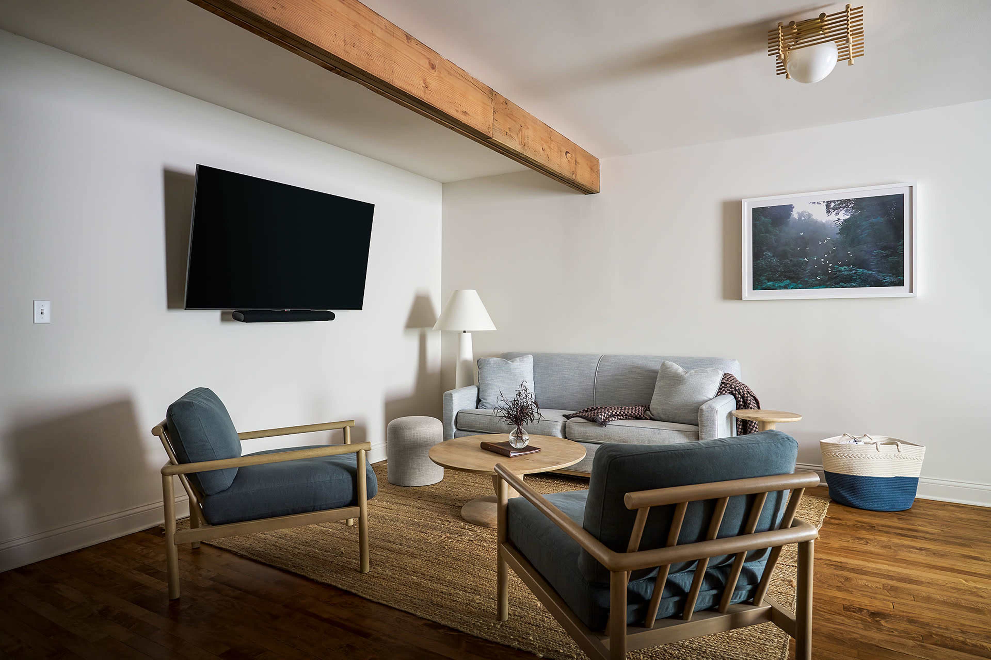 A modern living room with a gray sofa, two blue armchairs, a coffee table, and a mounted television on the wall.