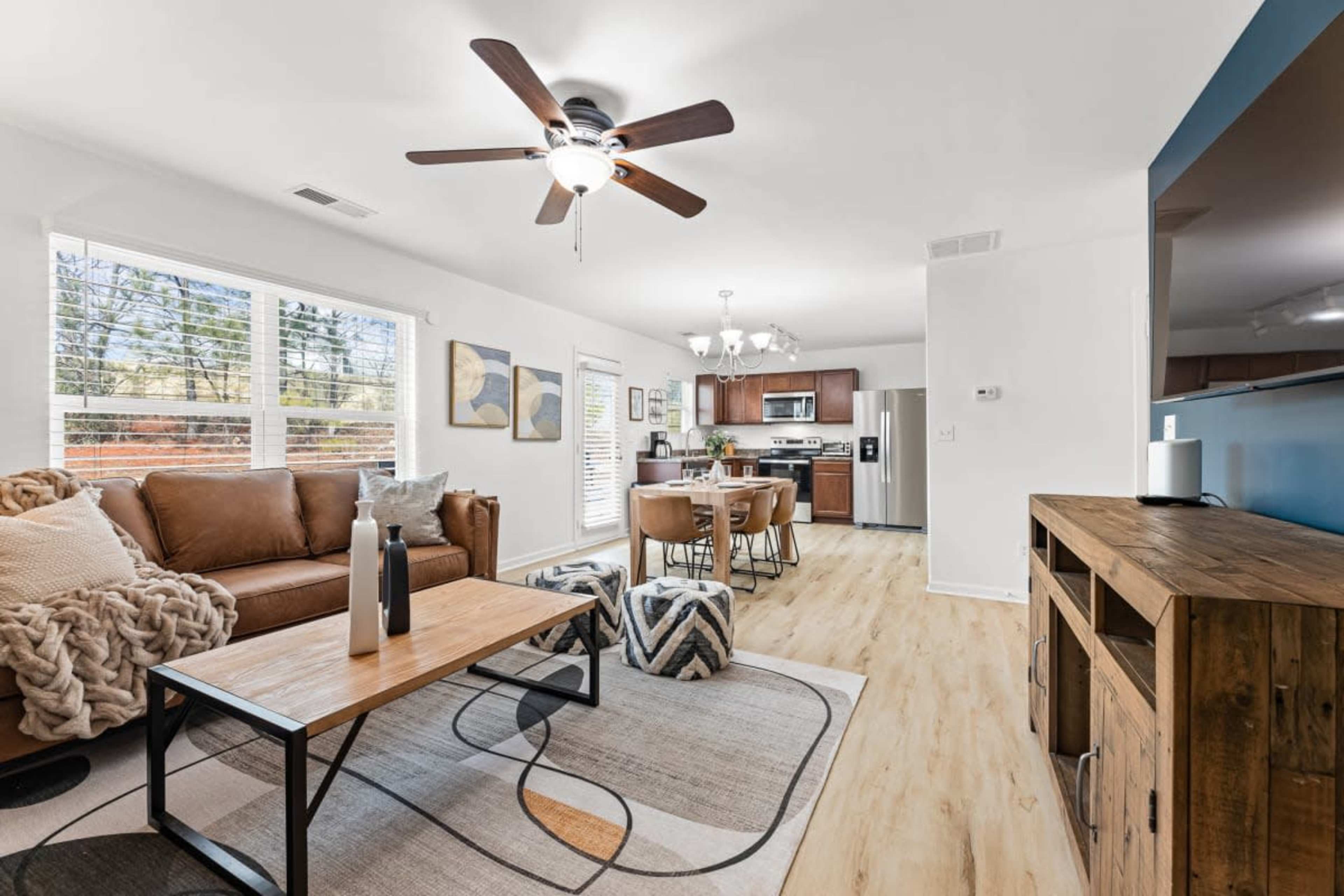 A modern living room features a brown leather sofa, a coffee table, and a dining area with a kitchen in the background.