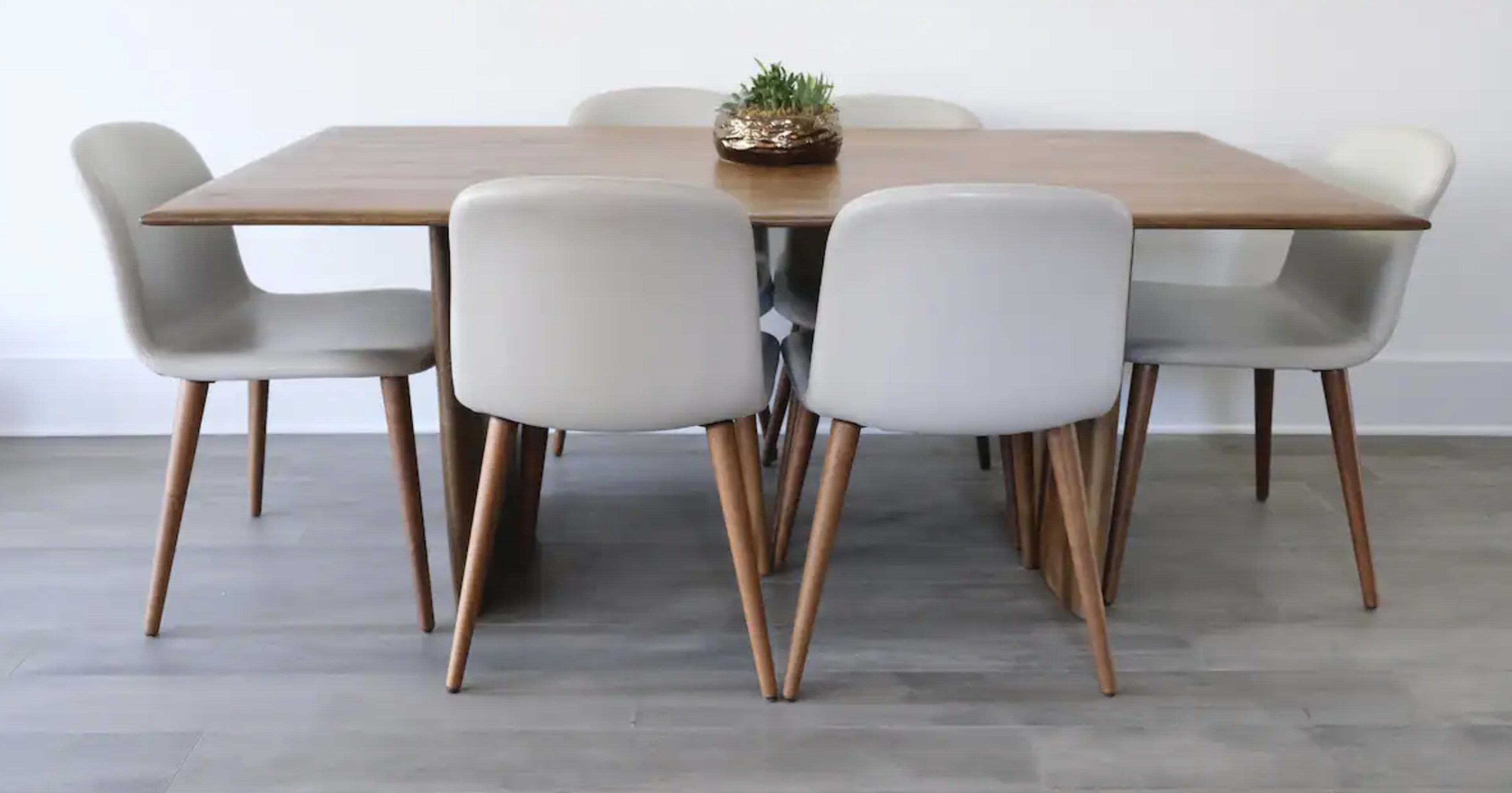 A wooden dining table is surrounded by five light-colored chairs with wooden legs, and a small decorative plant sits in the center.