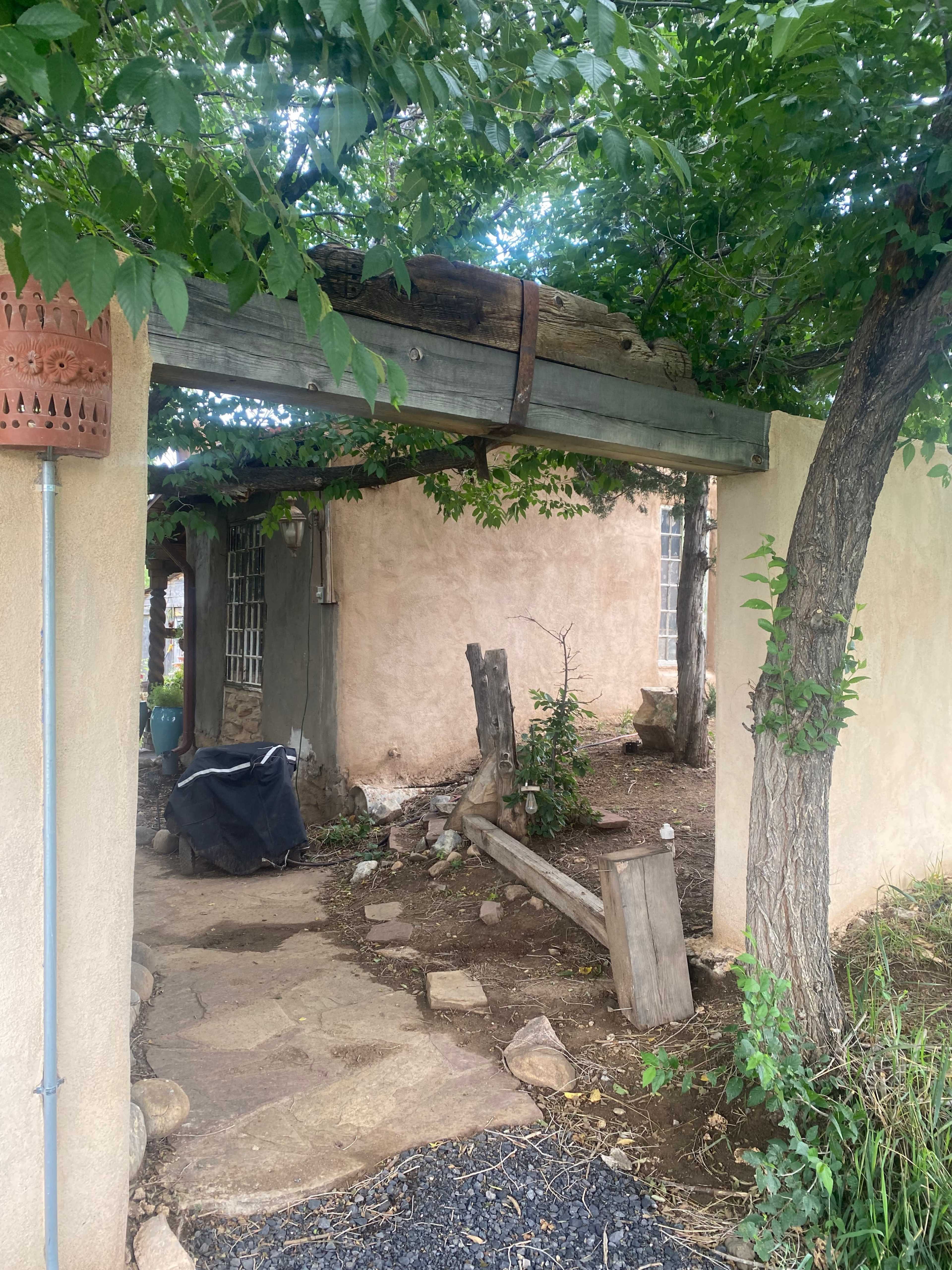 A weathered structure with a wooden pergola and a dirt path winds through greenery and stone.