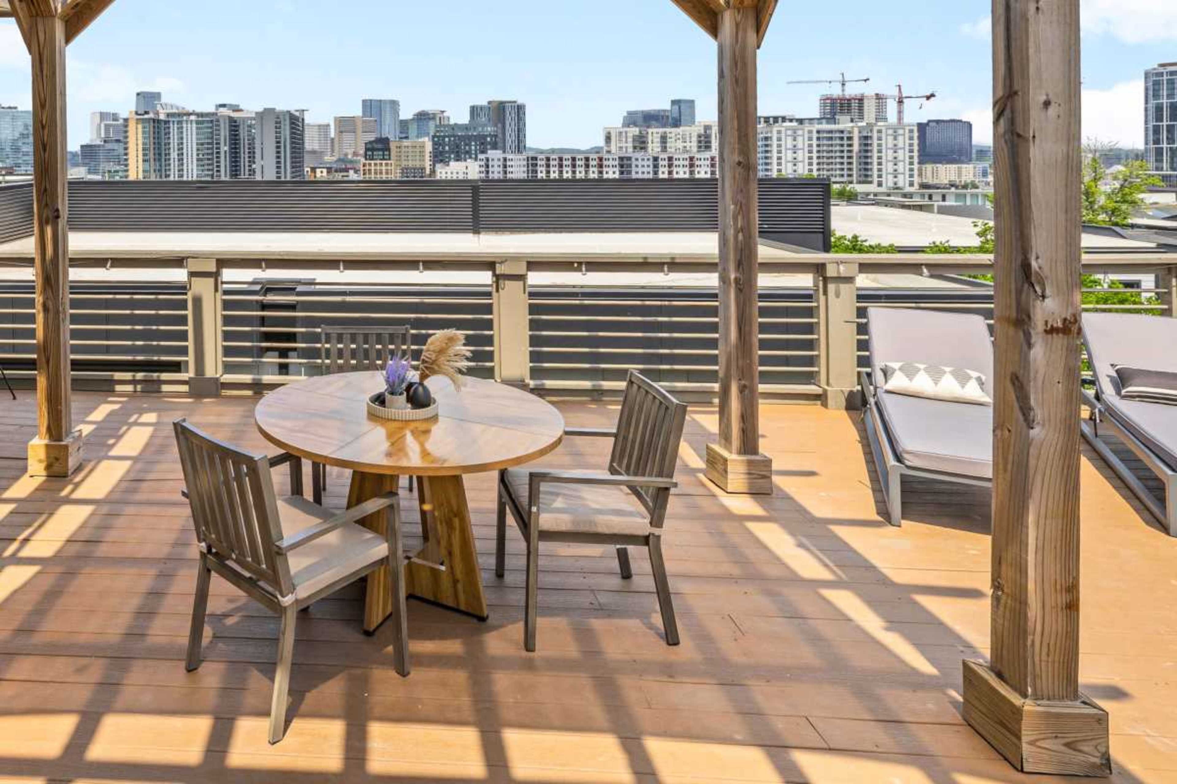 A wooden table with chairs is positioned on a deck, overlooking a city skyline with tall buildings in the background.