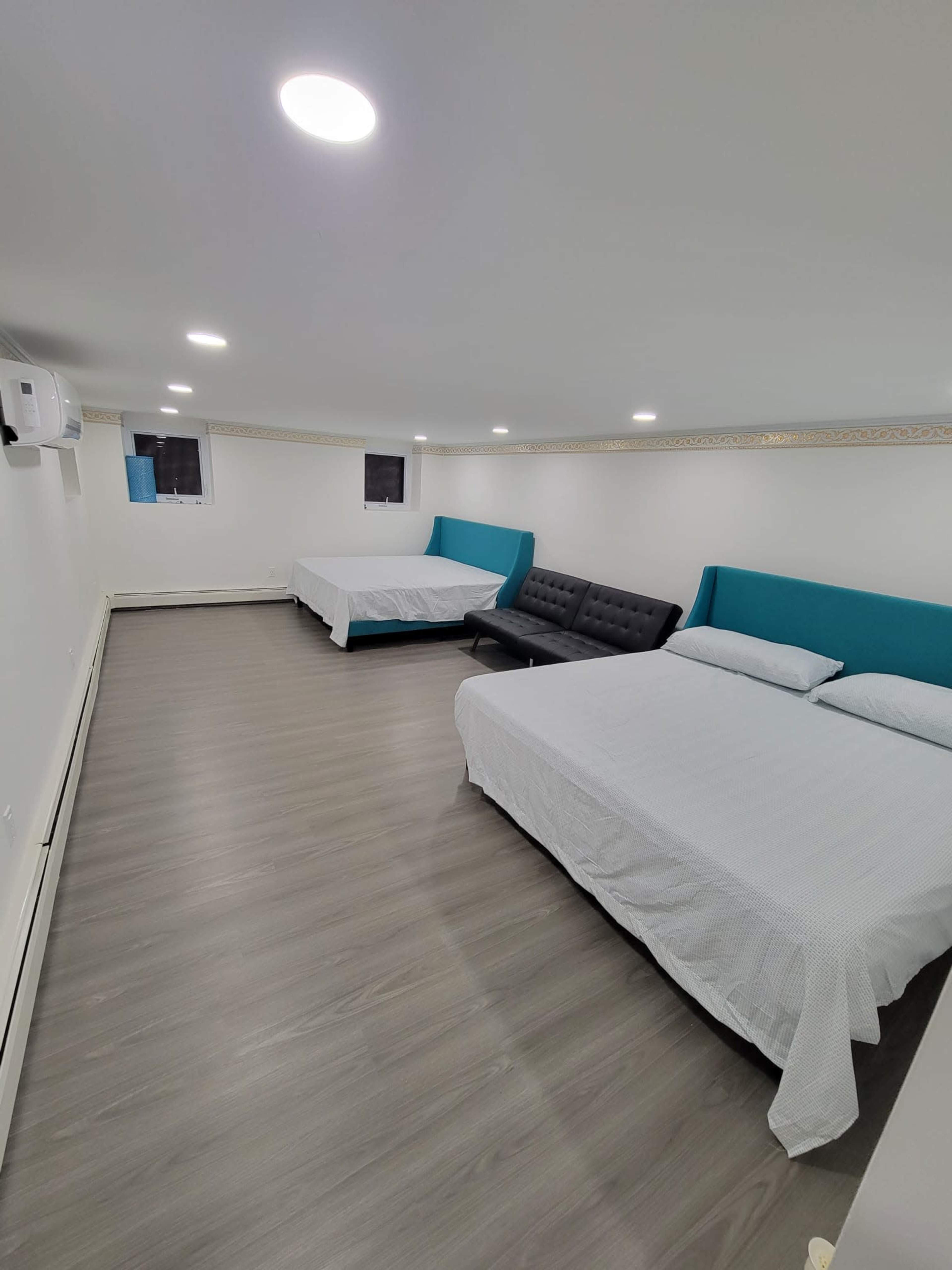 A spacious room with two beds, a sofa, and light-colored walls.