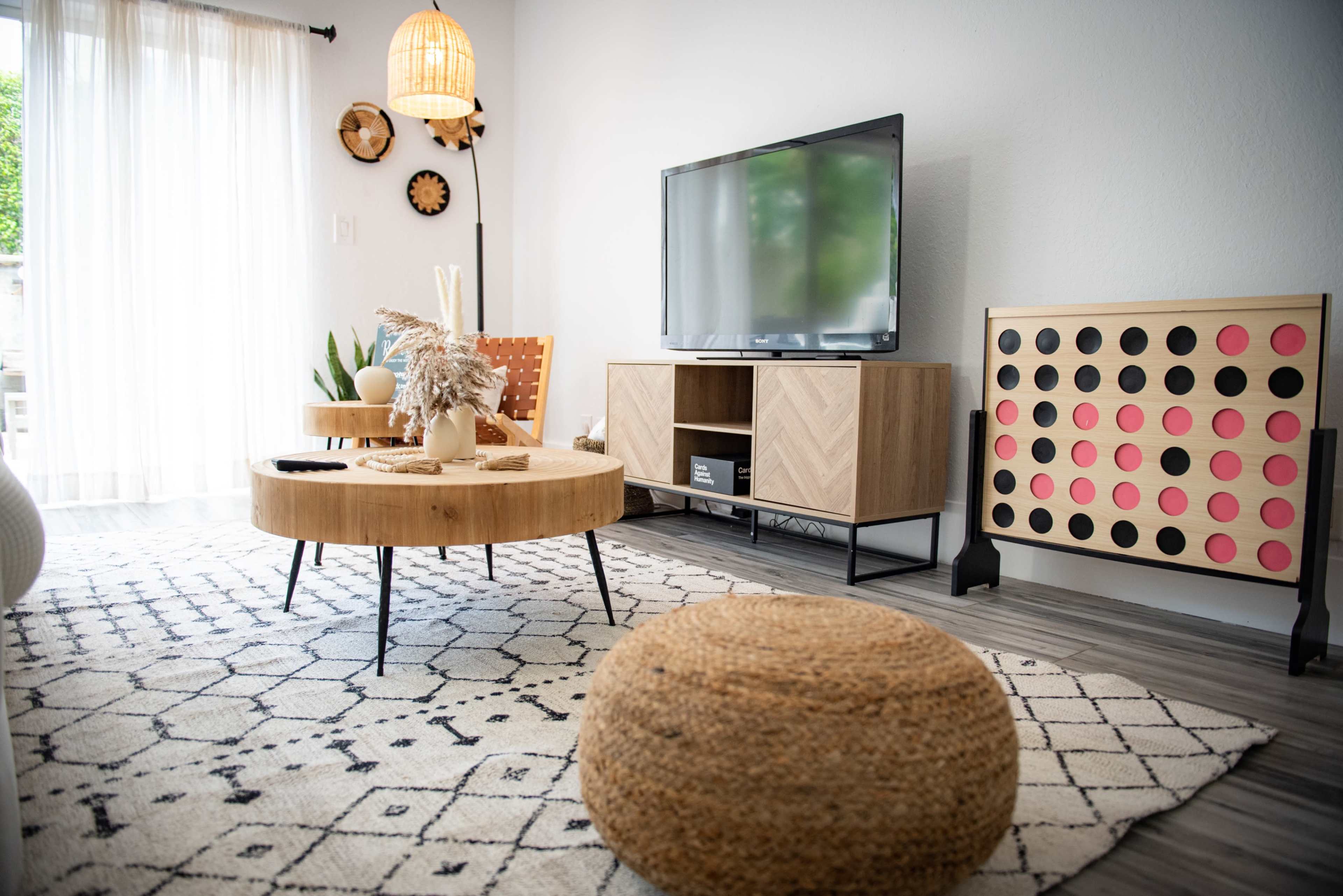 A modern living room with a circular wooden coffee table, a large television on a unit, and decorative elements like plants and a woven pouf.