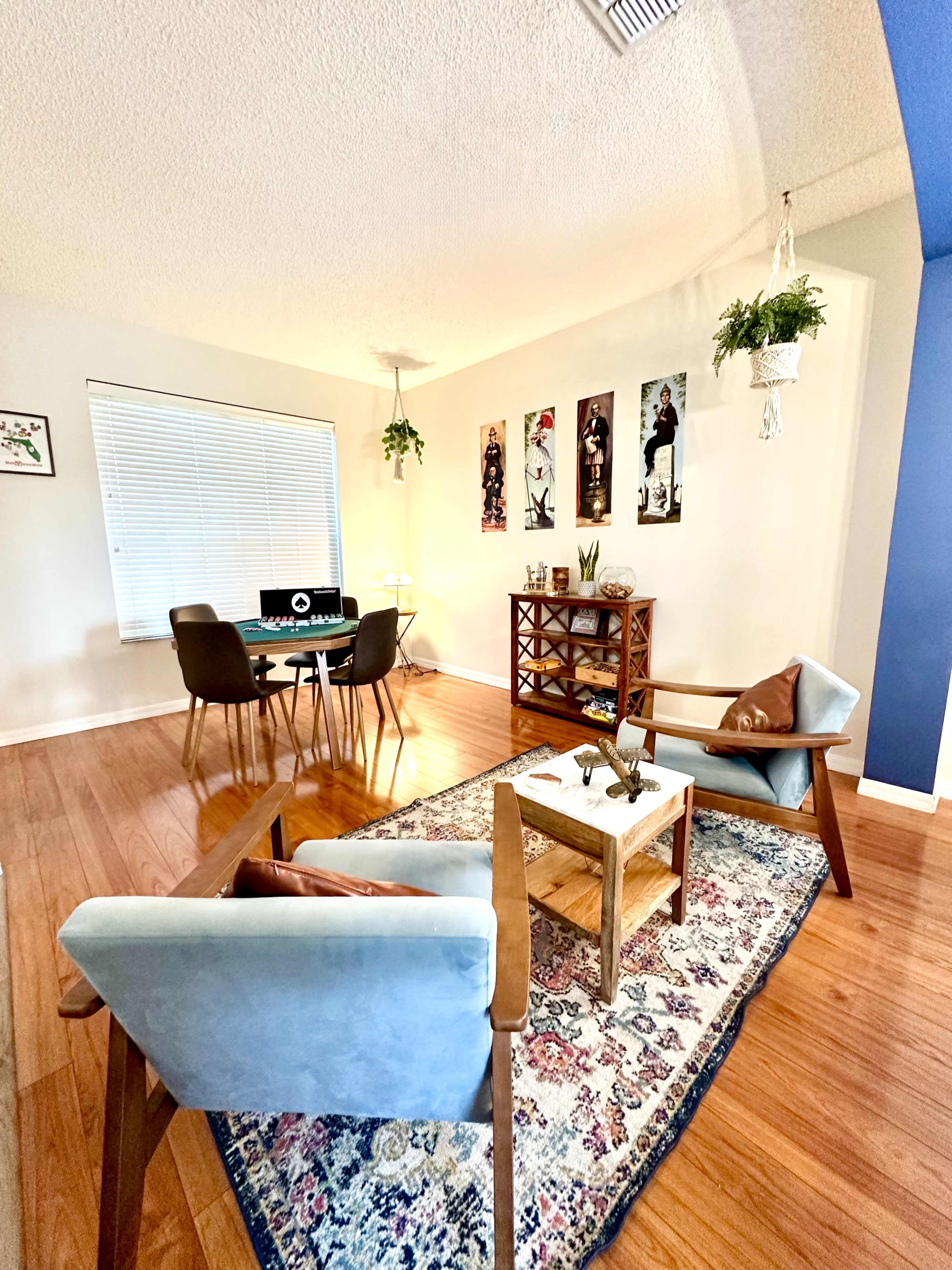 The image shows a modern living space featuring two armchairs, a small coffee table, a rug, and a dining area with a round table and chairs.