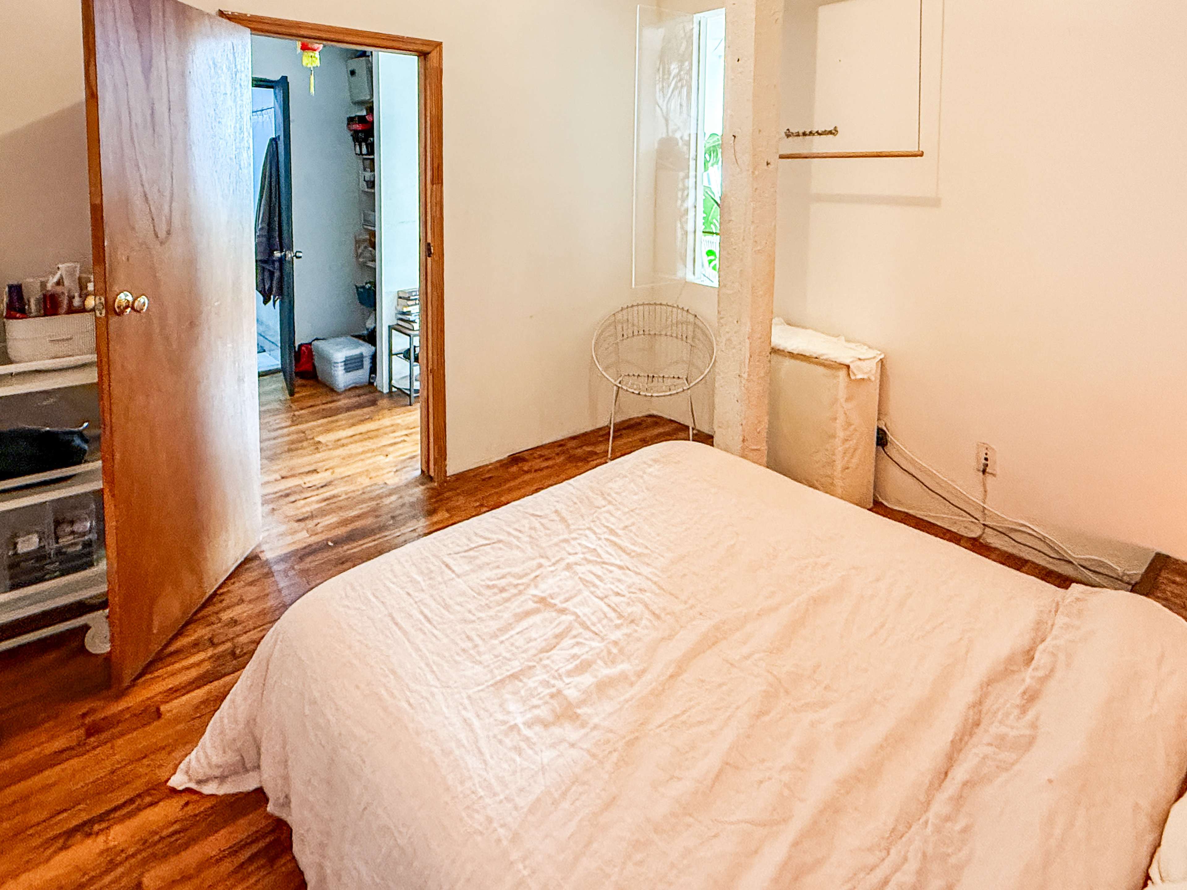 The image shows a simple bedroom with a bed, wooden flooring, and an open door leading to another room.