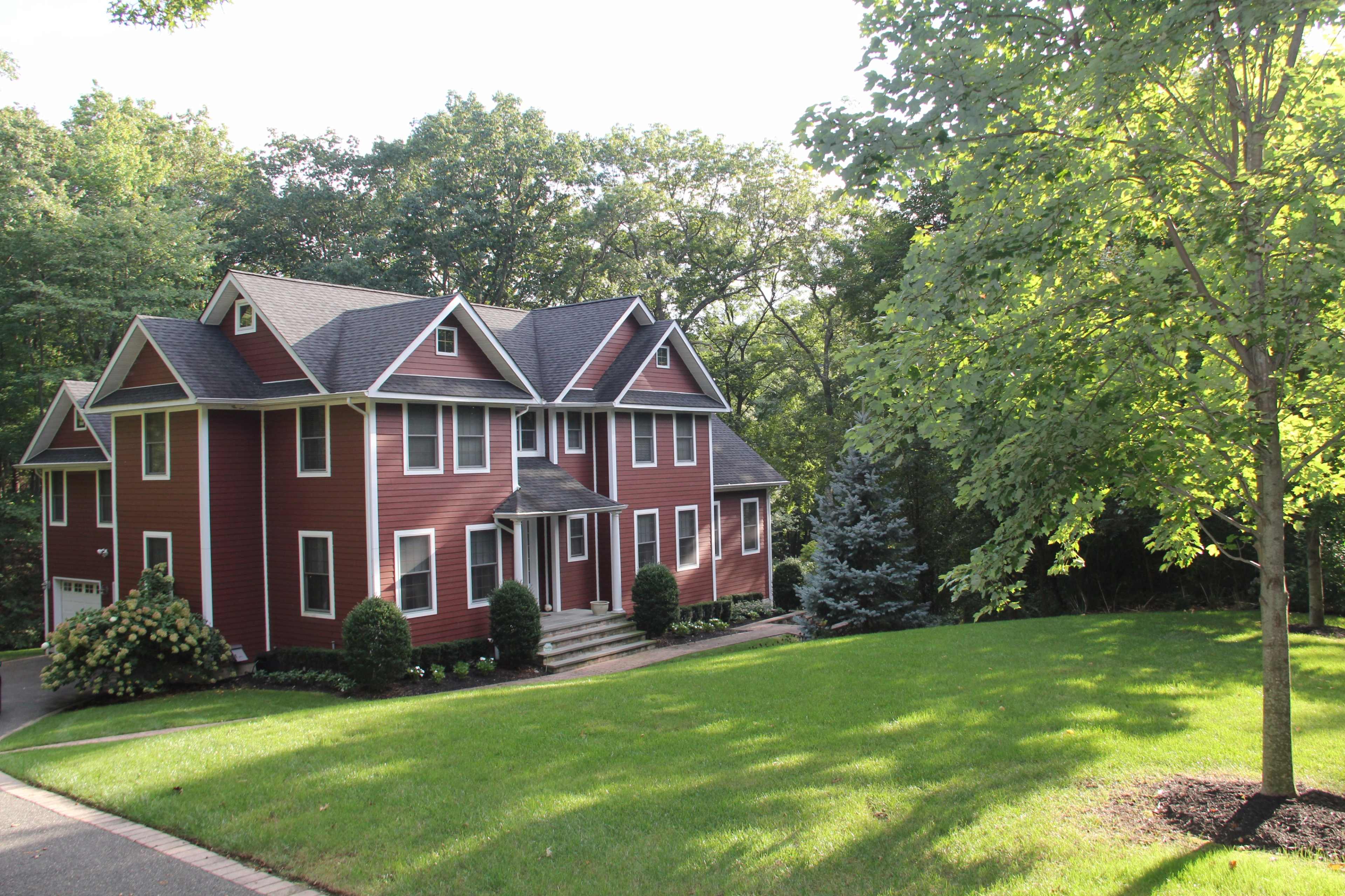 A large red house with multiple gabled roofs sits on a well-manicured lawn surrounded by trees.