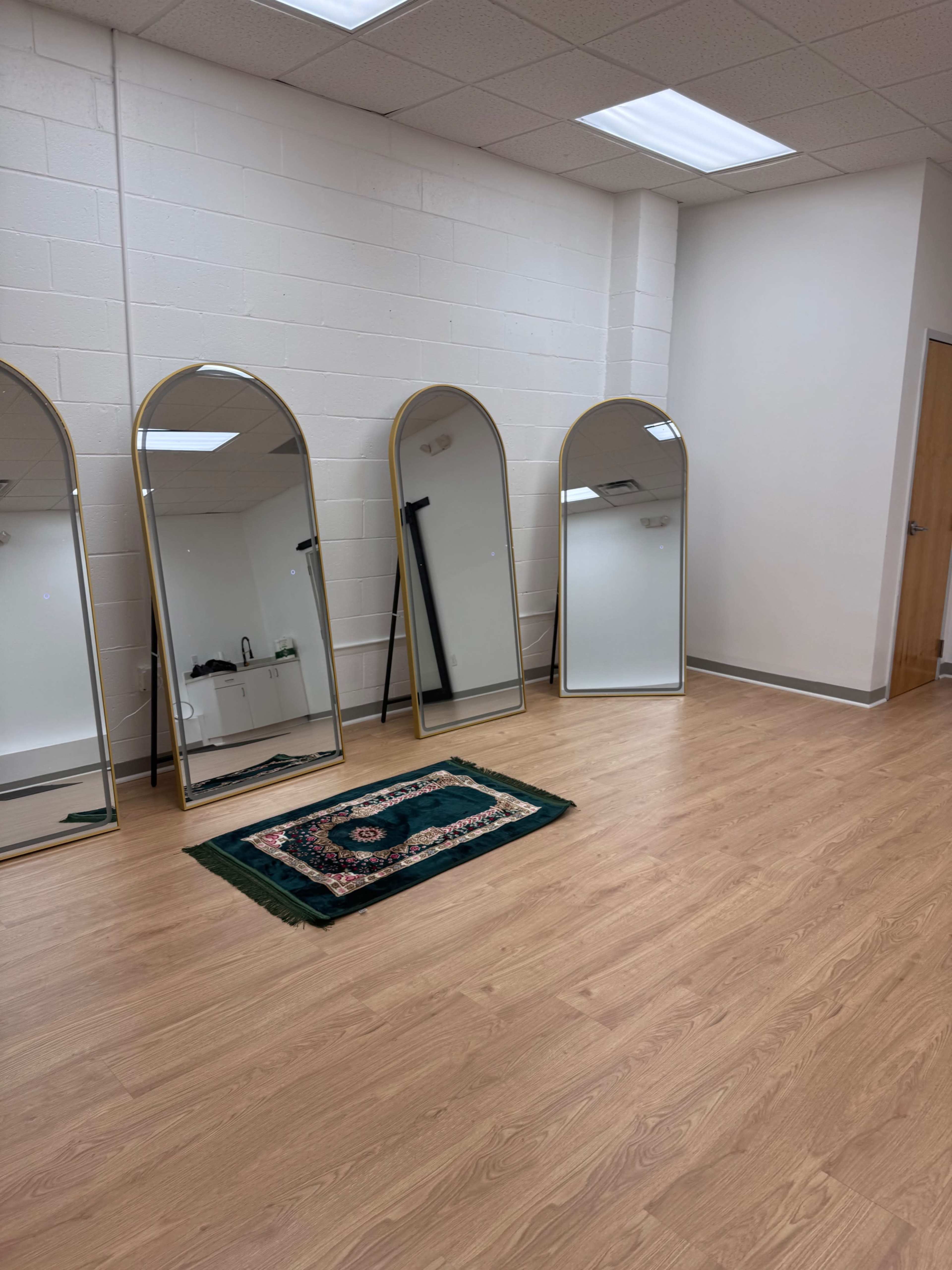 The image shows a spacious room with four tall, arched mirrors arranged in a line and a small area rug on the wooden floor.
