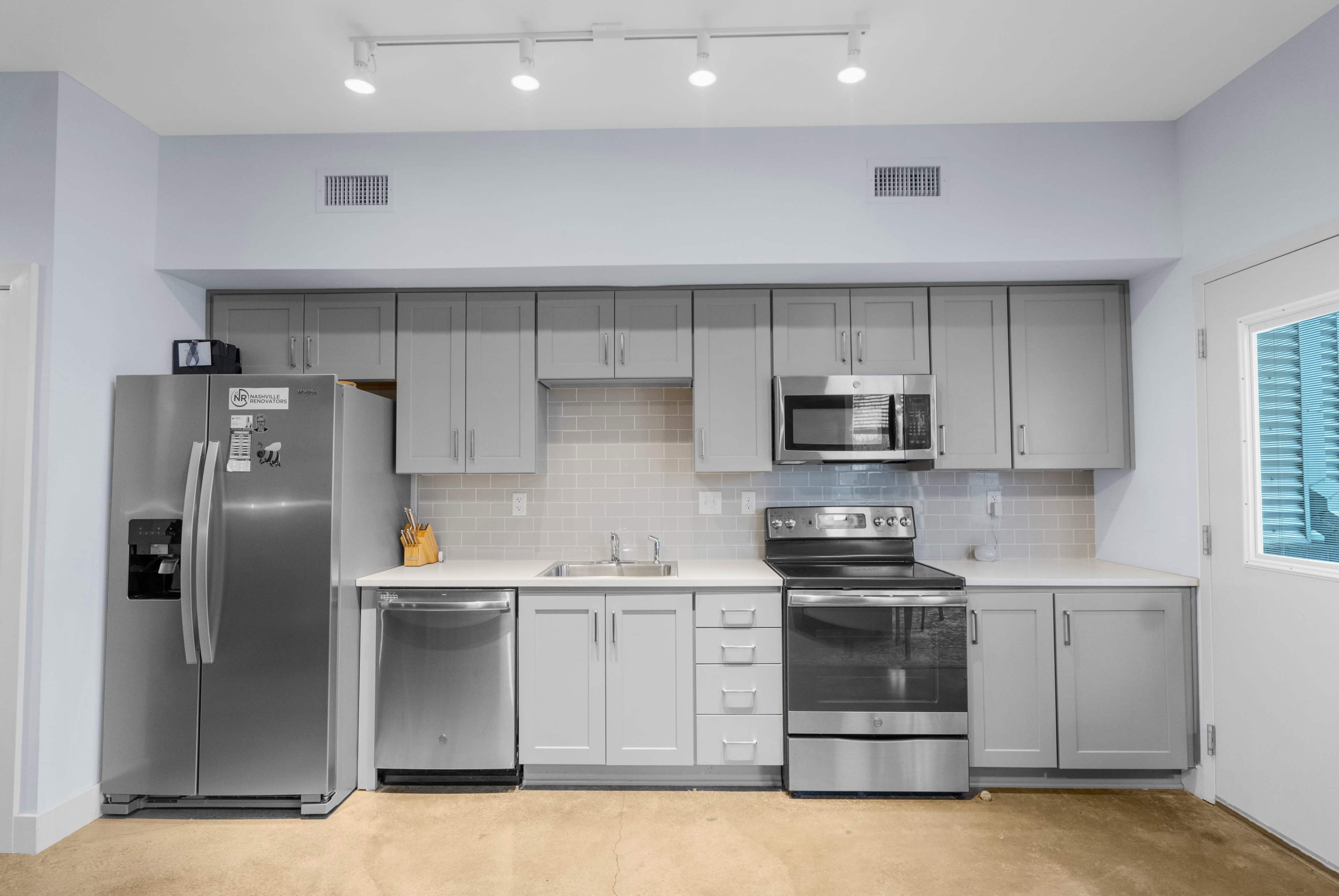 A modern kitchen features gray cabinets, stainless steel appliances, and a light-colored countertop with a backsplash.