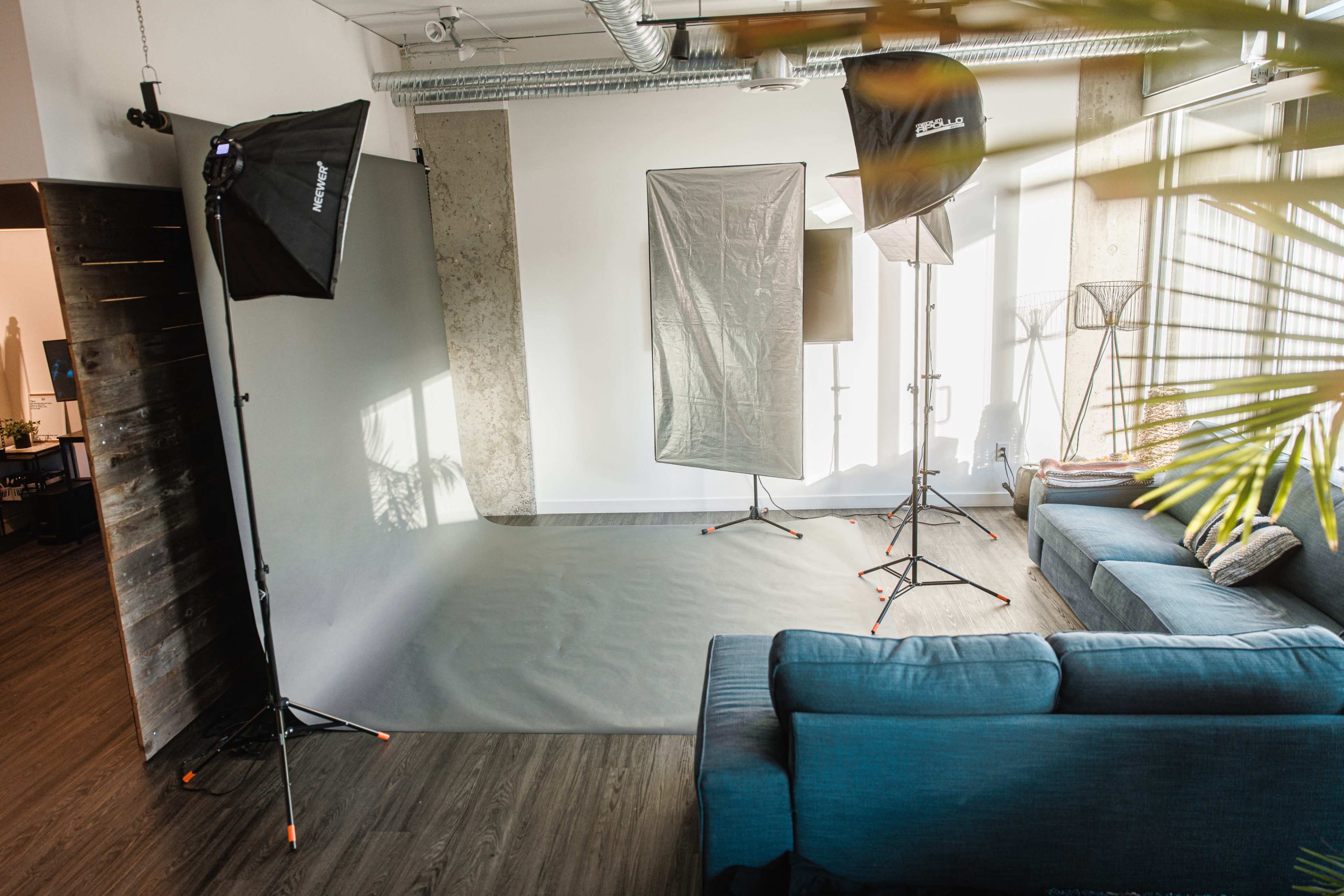 An indoor photography studio with softbox lights, a gray backdrop, and a couch in a well-lit room.