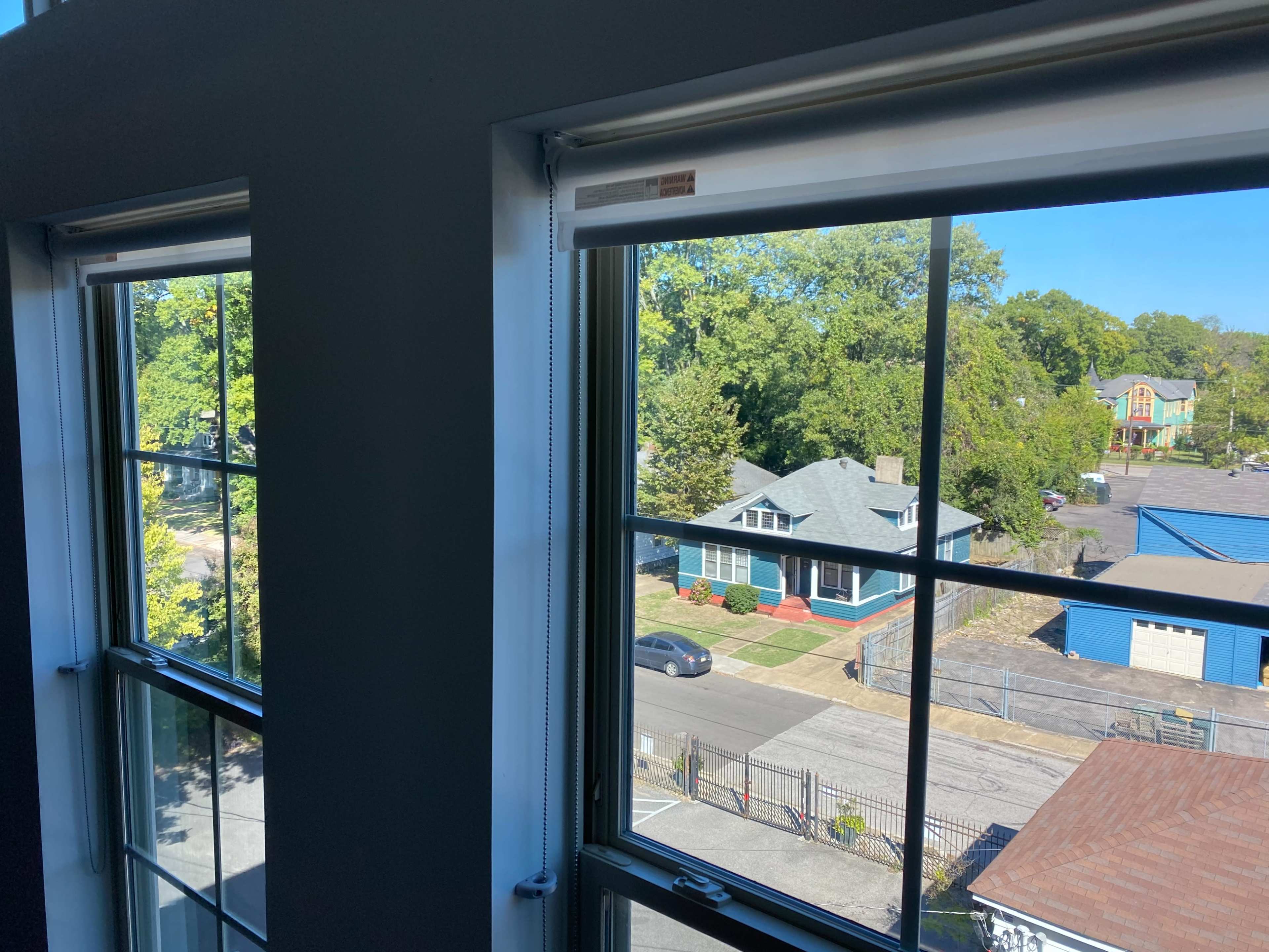 Two large windows frame a view of a neighborhood with houses, trees, and streets on a clear day.