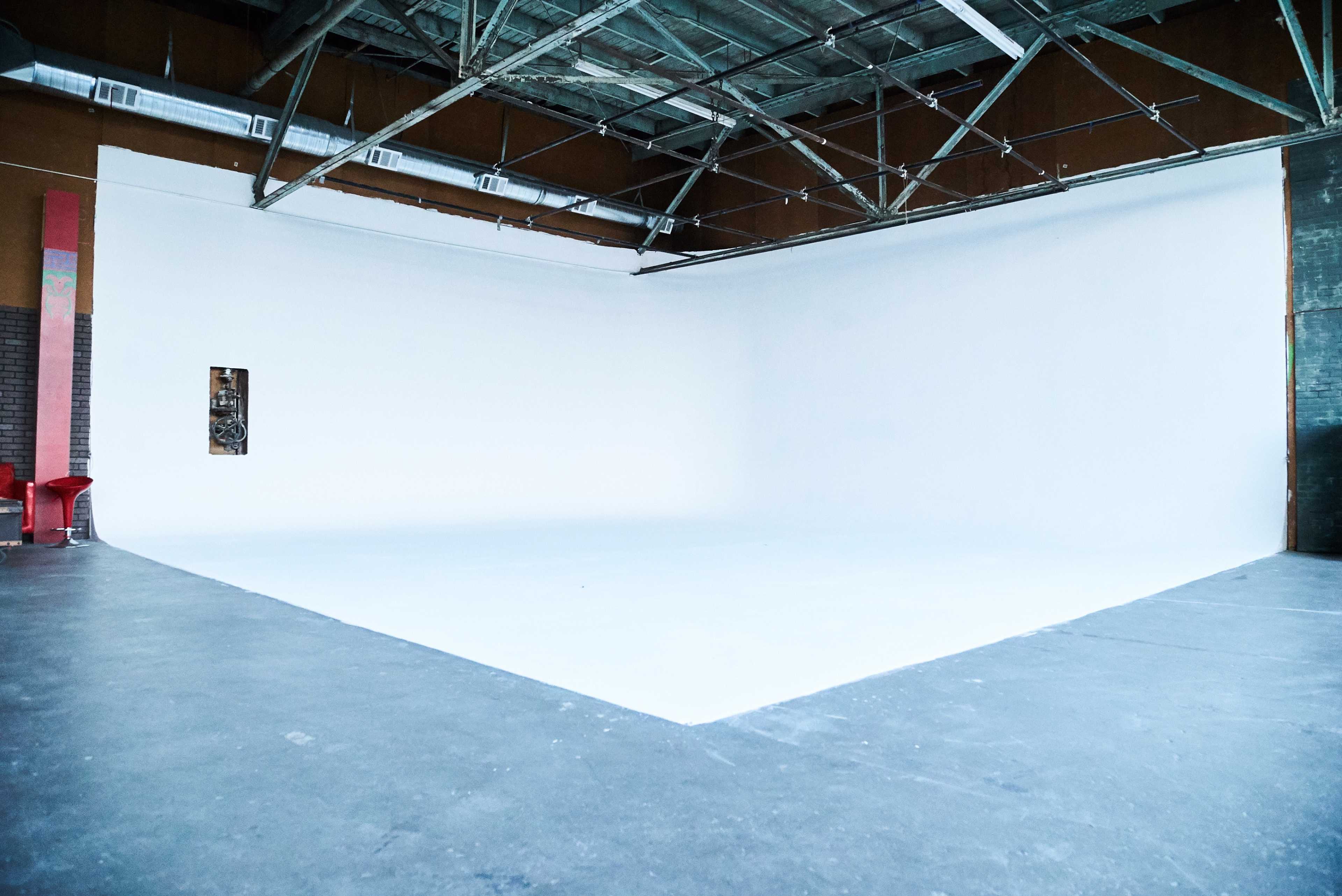 A spacious studio with a large, empty white wall and a concrete floor.