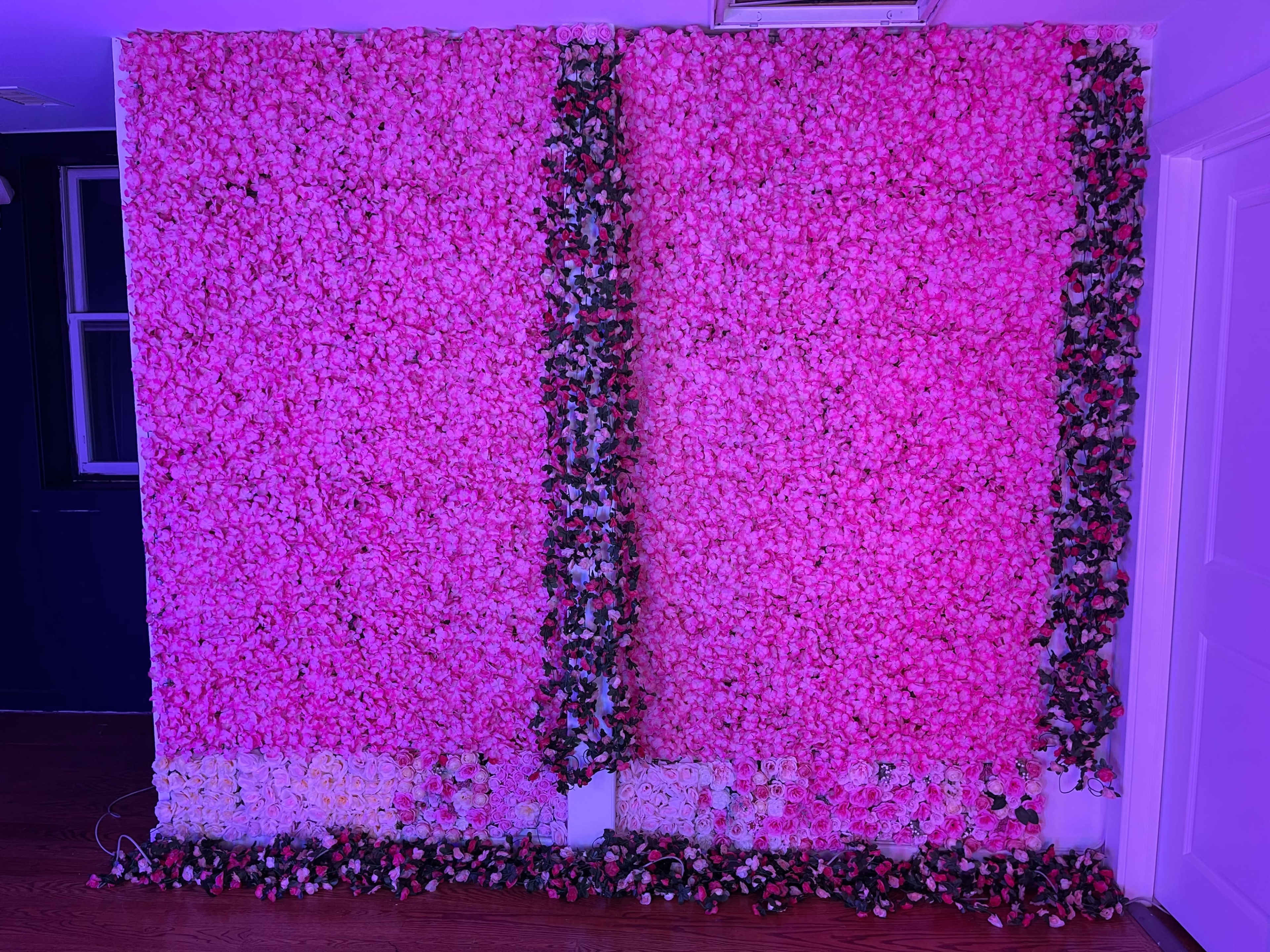 A brightly lit wall covered with pink artificial flowers and greenery.