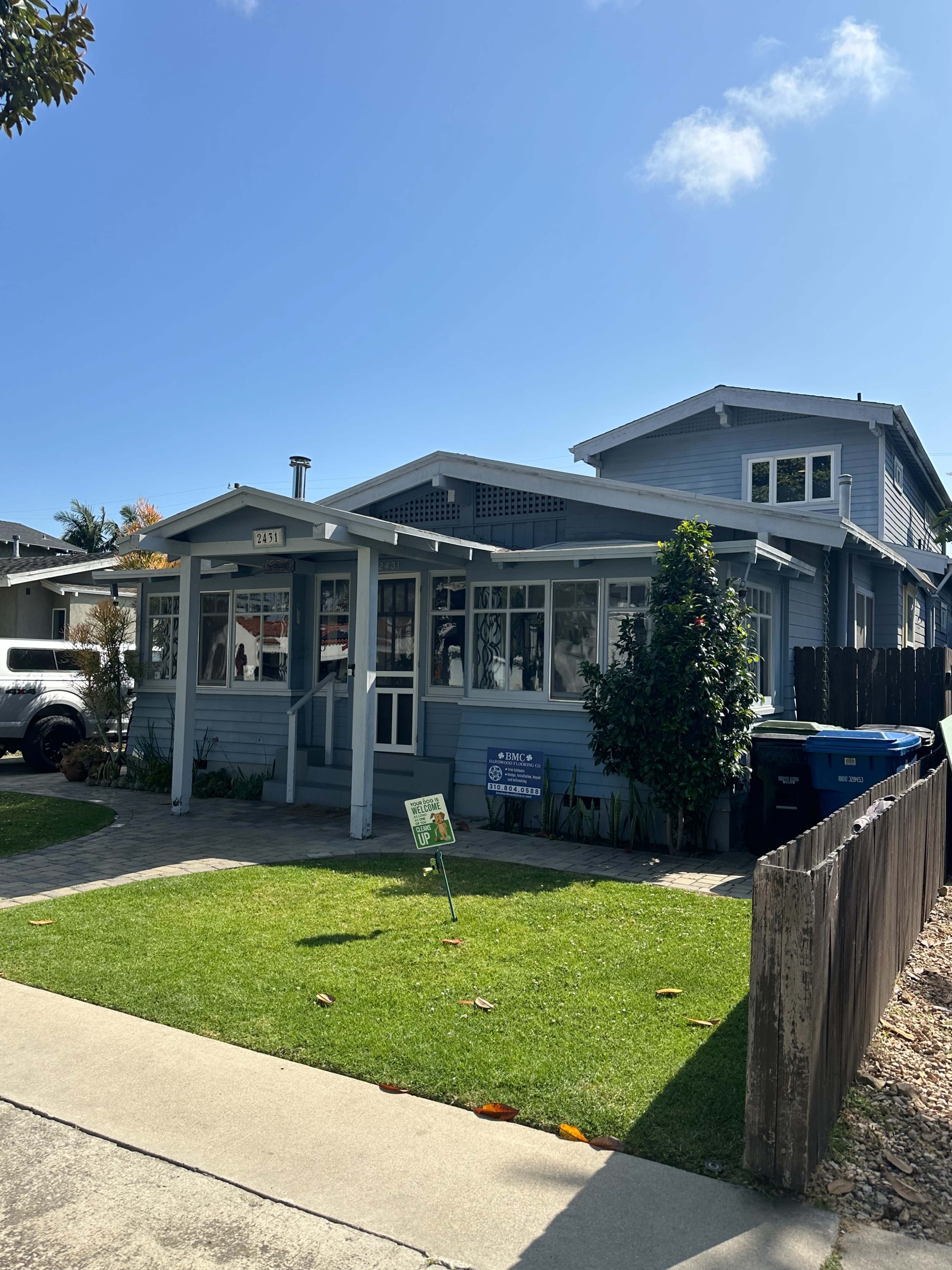 A light blue single-story house with a front porch is surrounded by a well-maintained lawn and a gravel pathway.
