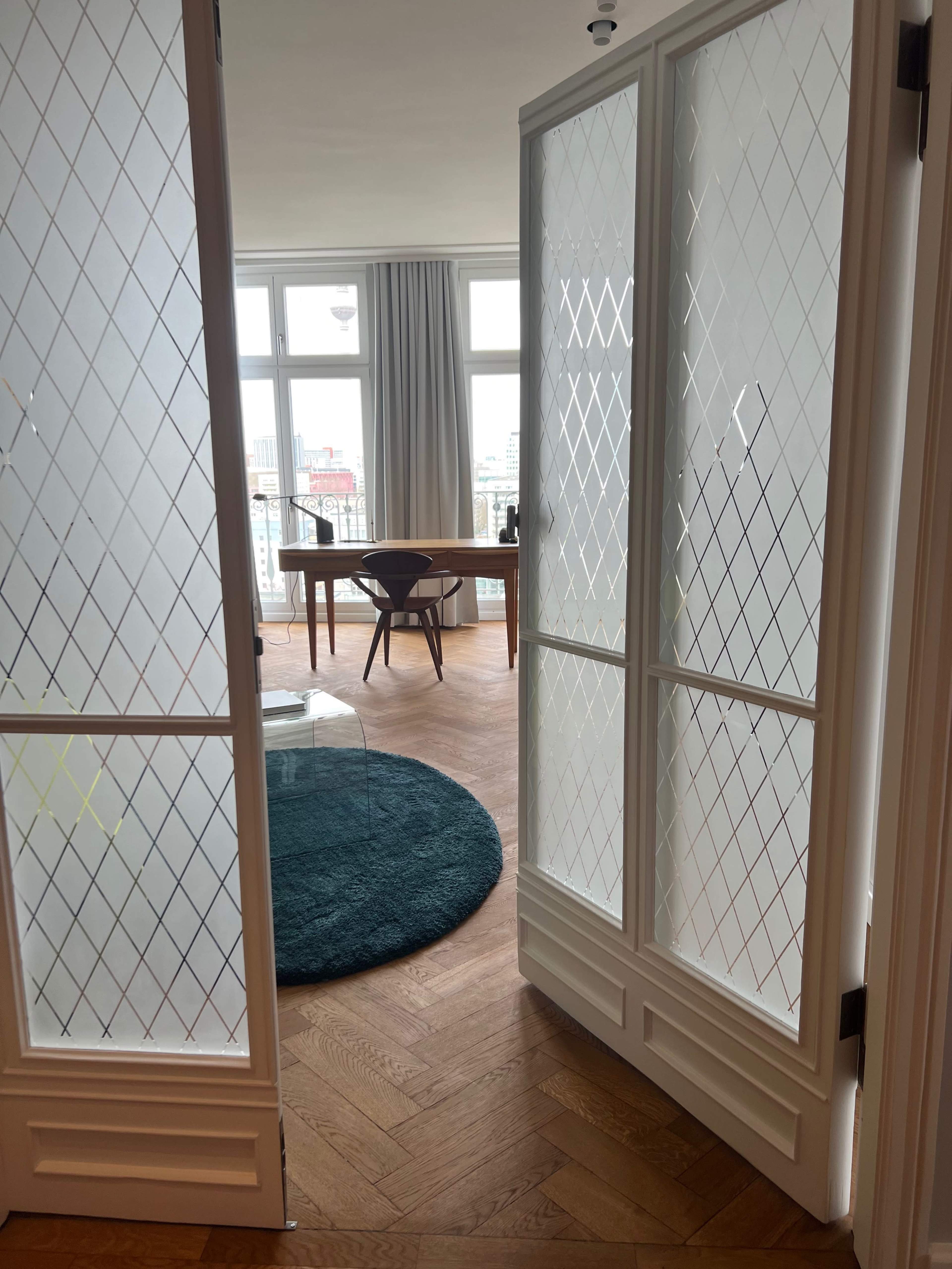 A pair of glass-paneled doors opens to reveal a modern workspace with a wooden desk and a round rug.