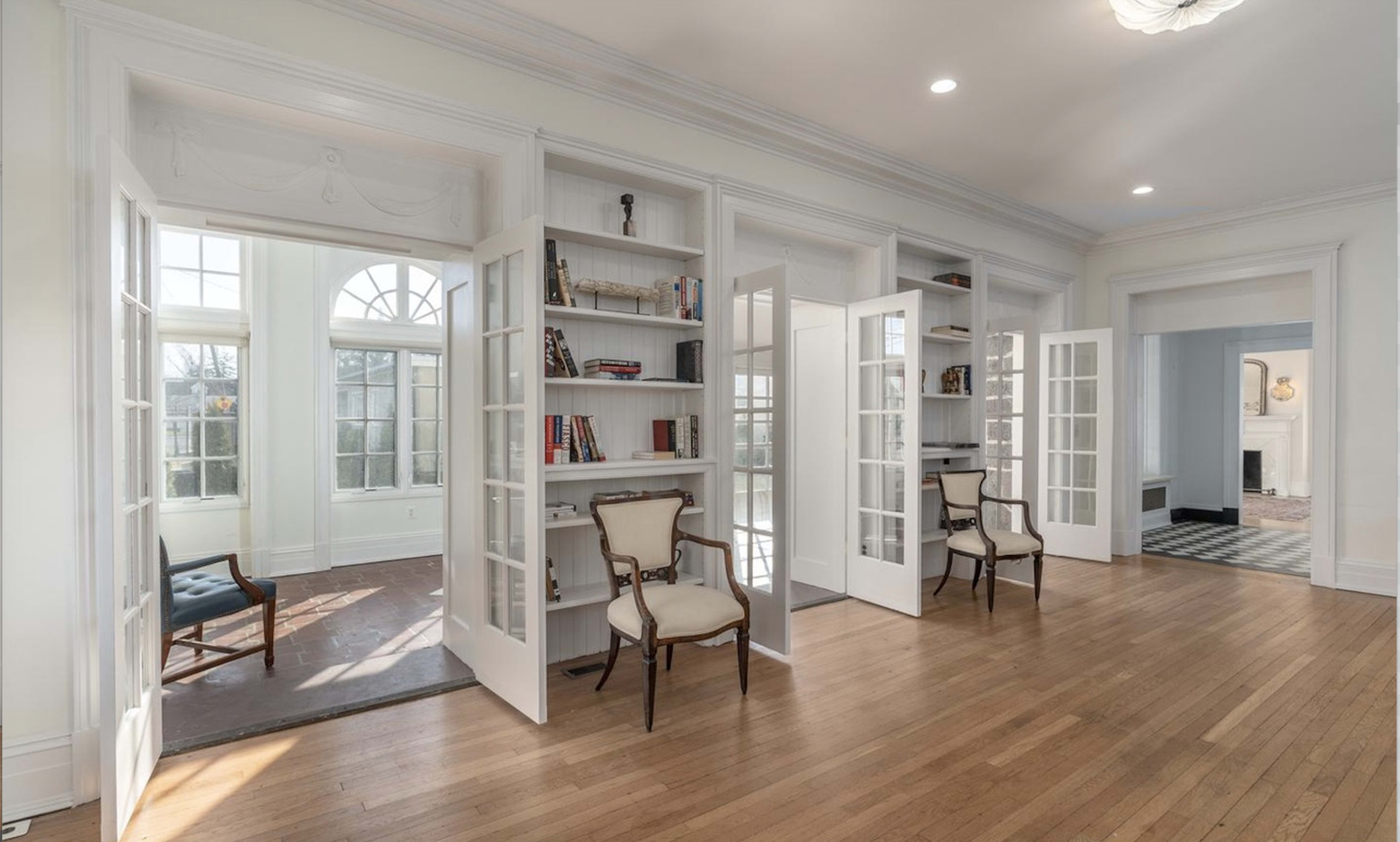 A bright, spacious room with white walls, a built-in bookshelf, double doors, and two wooden chairs.