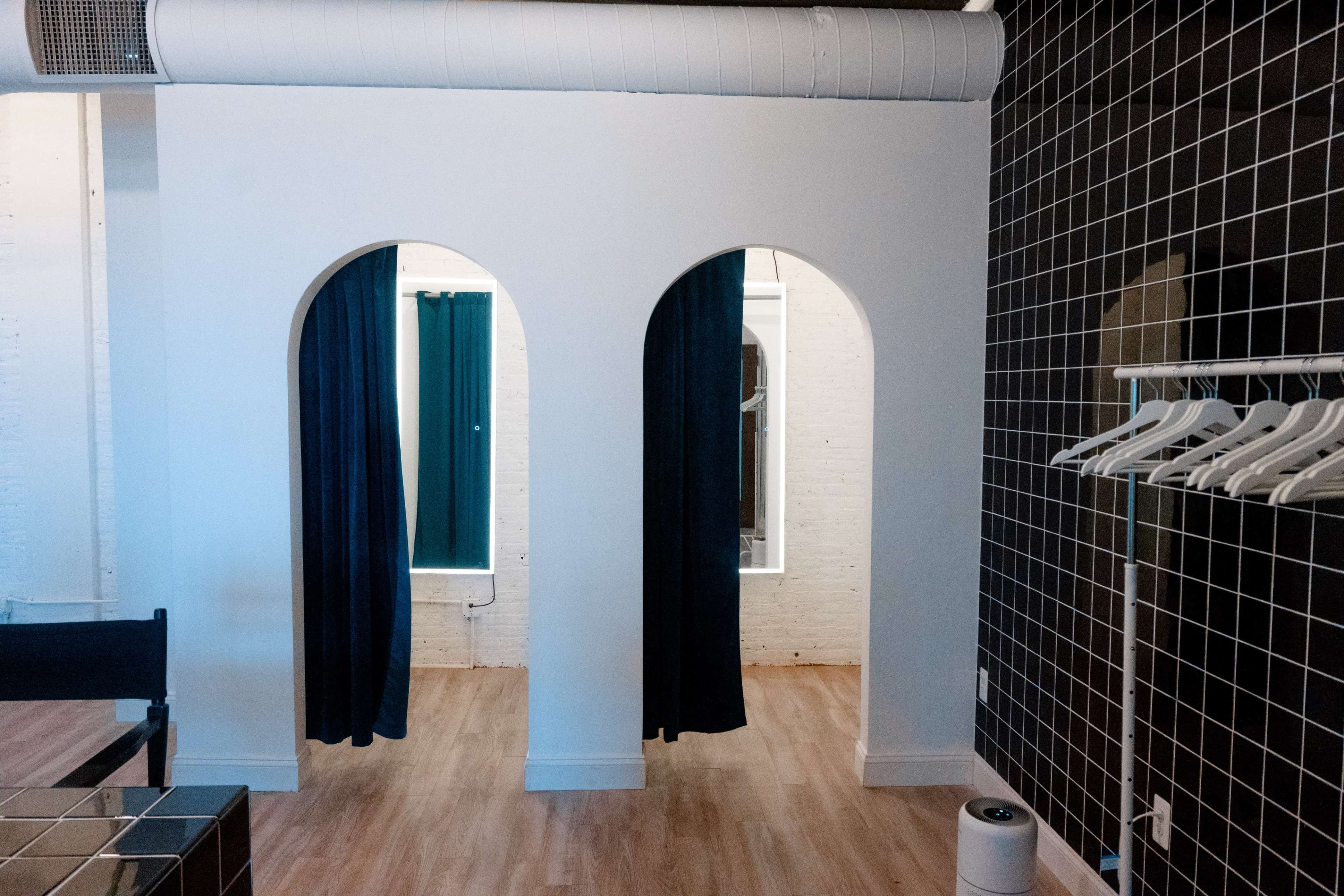 A bright interior space featuring two arched dressing room entrances with dark curtains, surrounded by white walls and tiled accents.