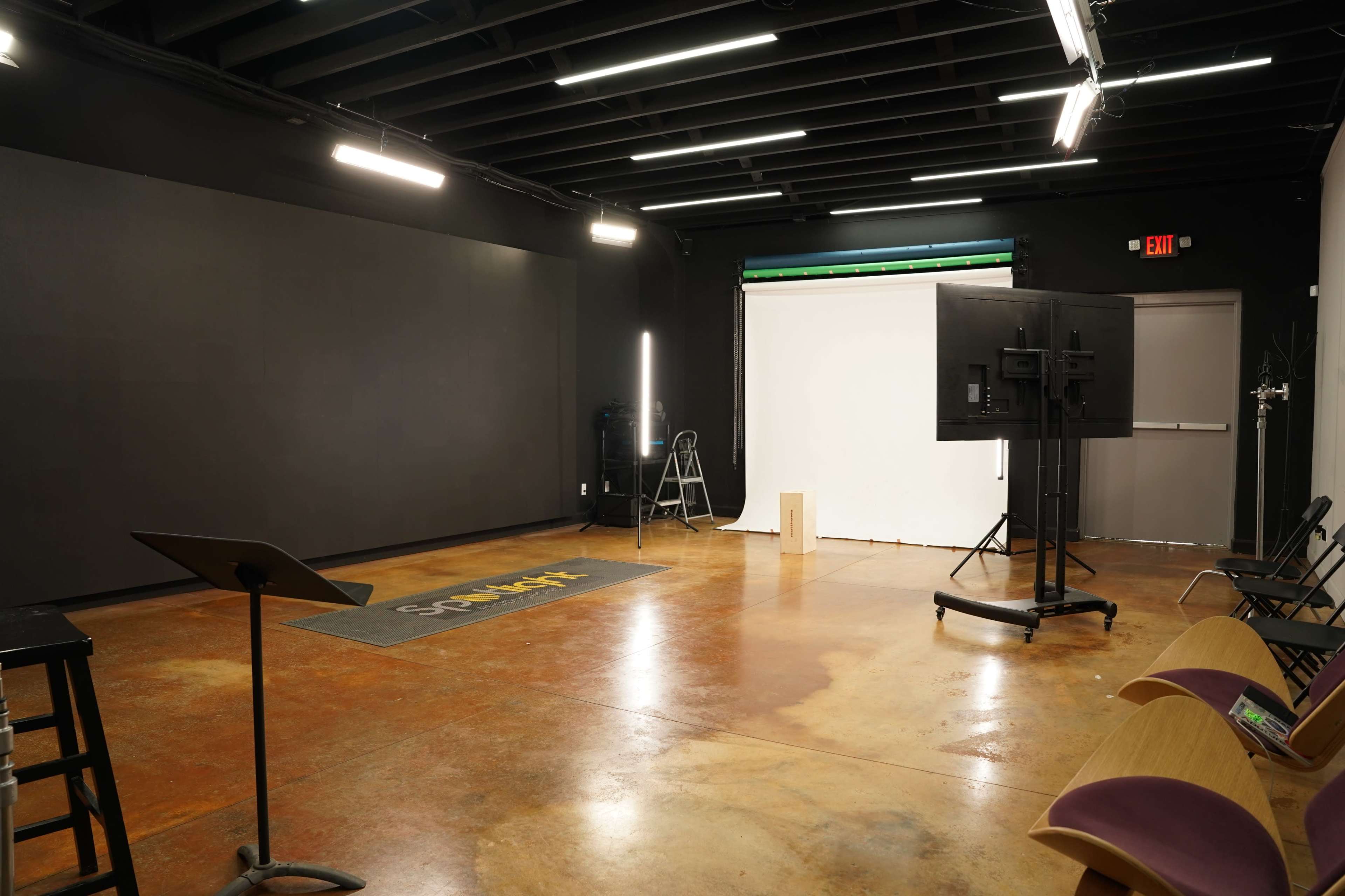 An empty studio space with a polished concrete floor, a black backdrop, and lighting equipment arranged for a photoshoot or presentation.