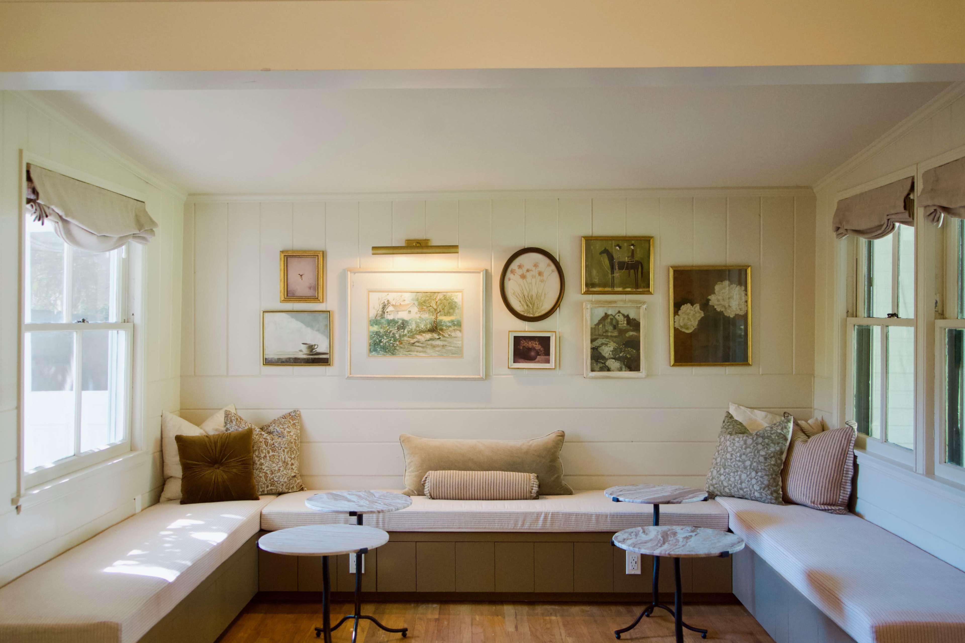 A bright room features a built-in seating area with decorative pillows and several framed artworks on the wall.