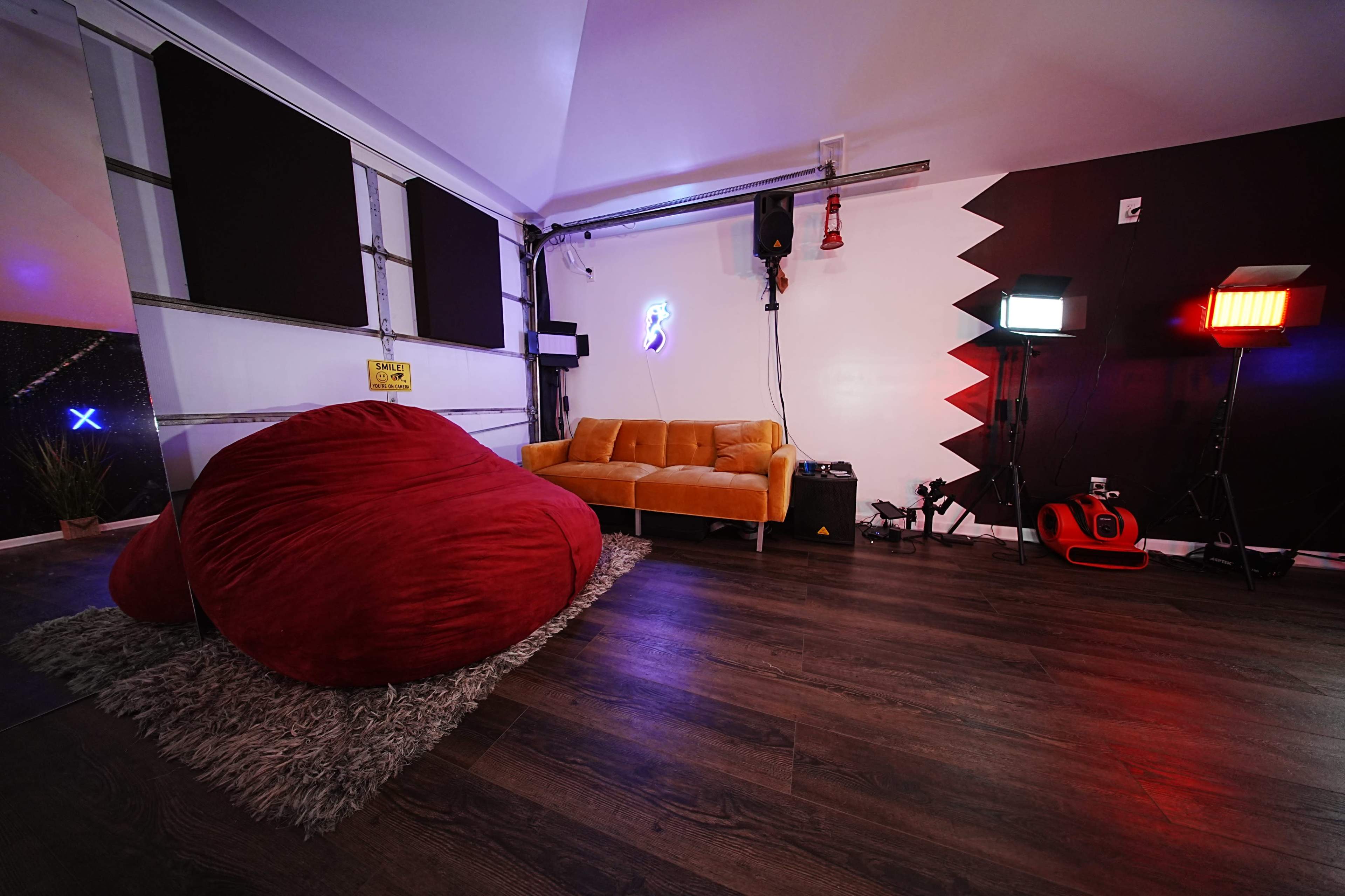 The image shows a room with a large red bean bag, a yellow couch, and studio lighting set up in a corner.