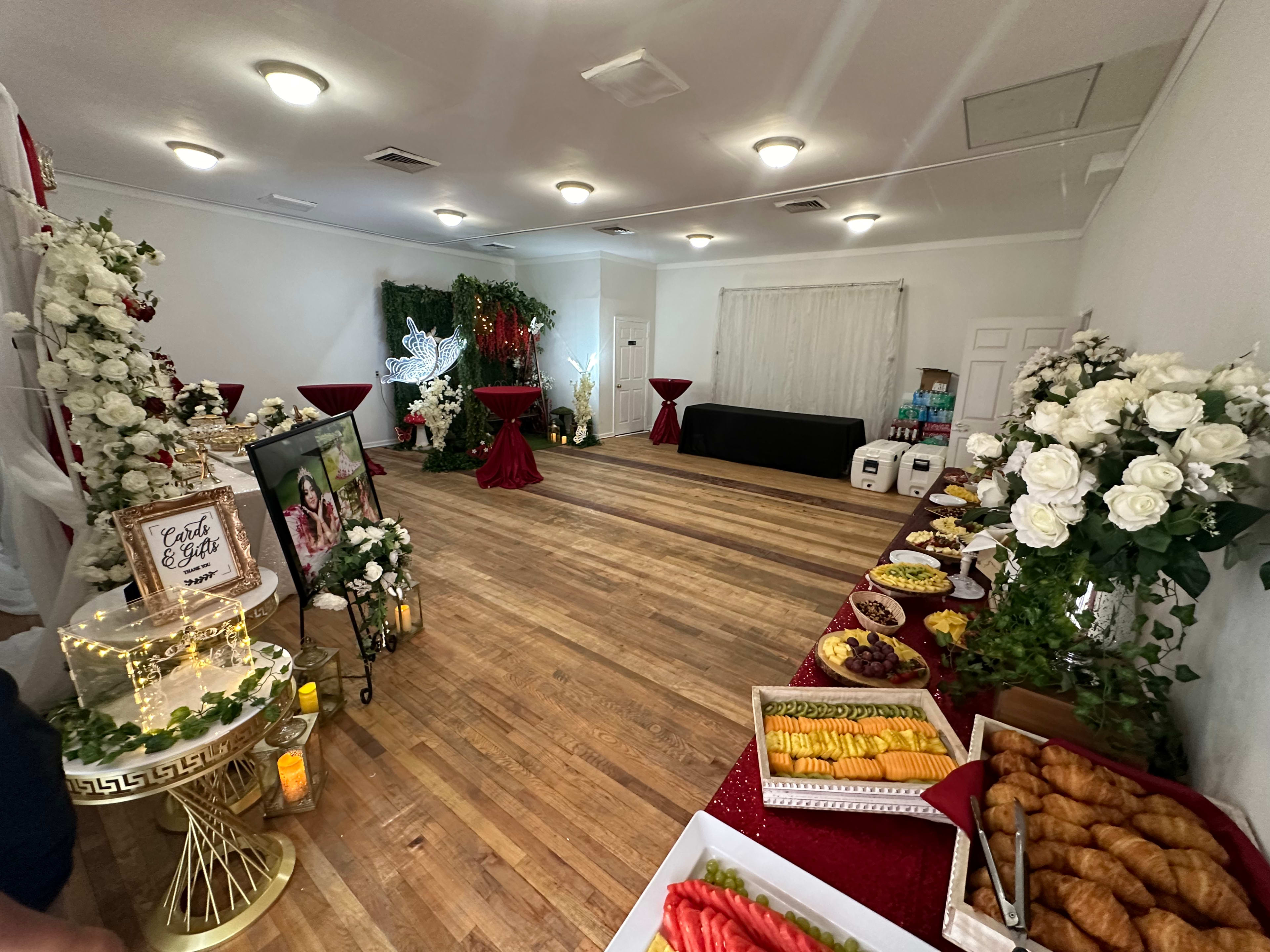 An elegantly decorated event space with tables adorned with red tablecloths, floral arrangements, and a variety of food displayed along one side.