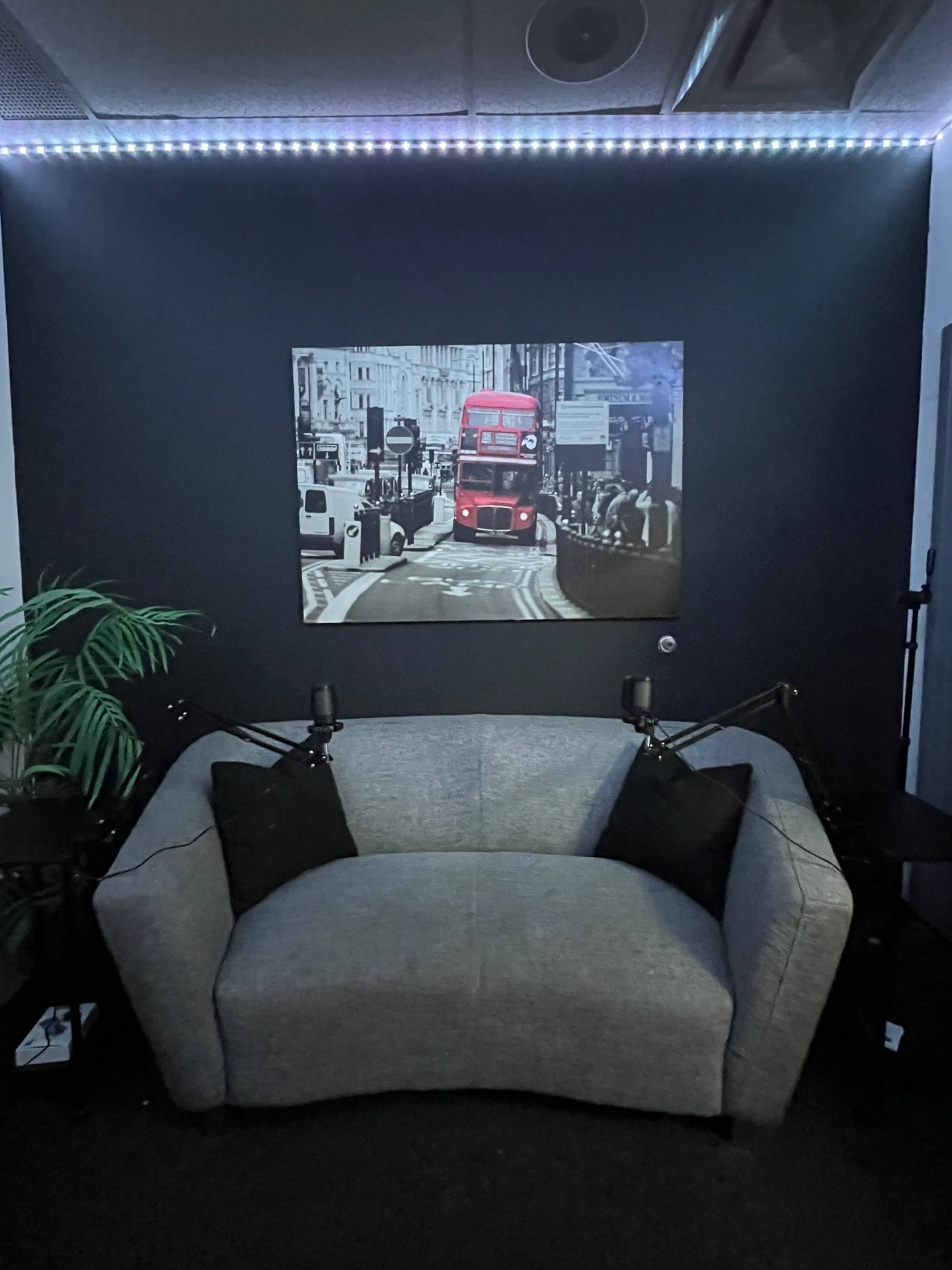 A gray couch with decorative black pillows in front of a wall featuring a black-and-white photograph of a red bus in a city street, illuminated by LED lights.