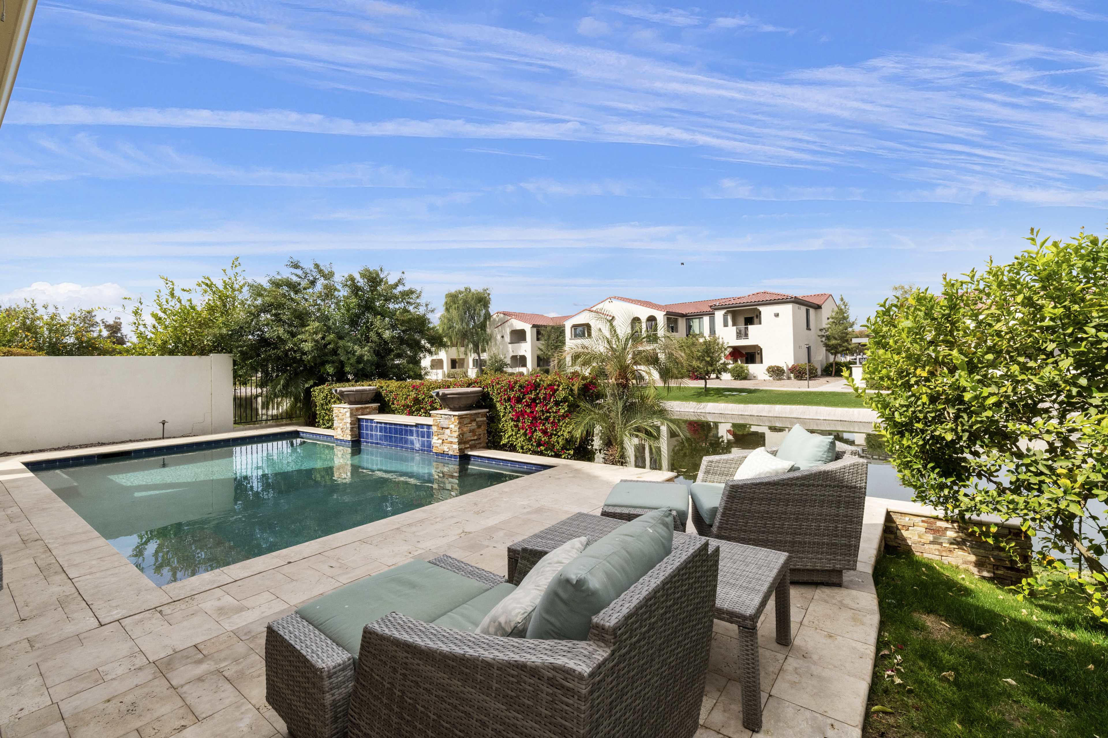 The image shows a backyard featuring a swimming pool surrounded by lounge chairs, with a landscaped area and residential buildings in the background.