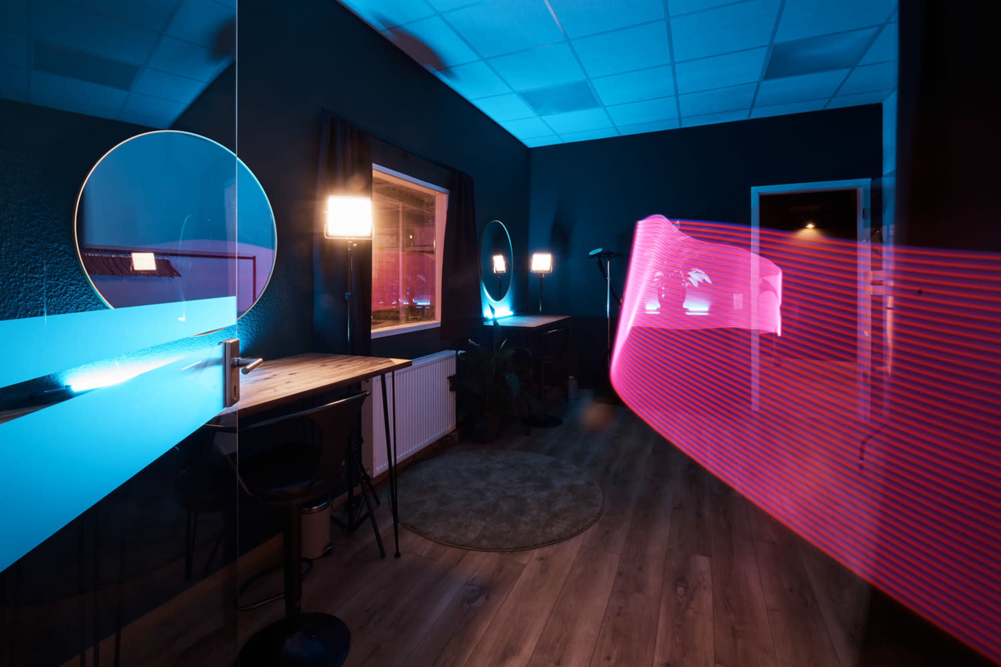 A modern room features round mirrors, a wooden table, and ambient lighting in blue and pink tones.