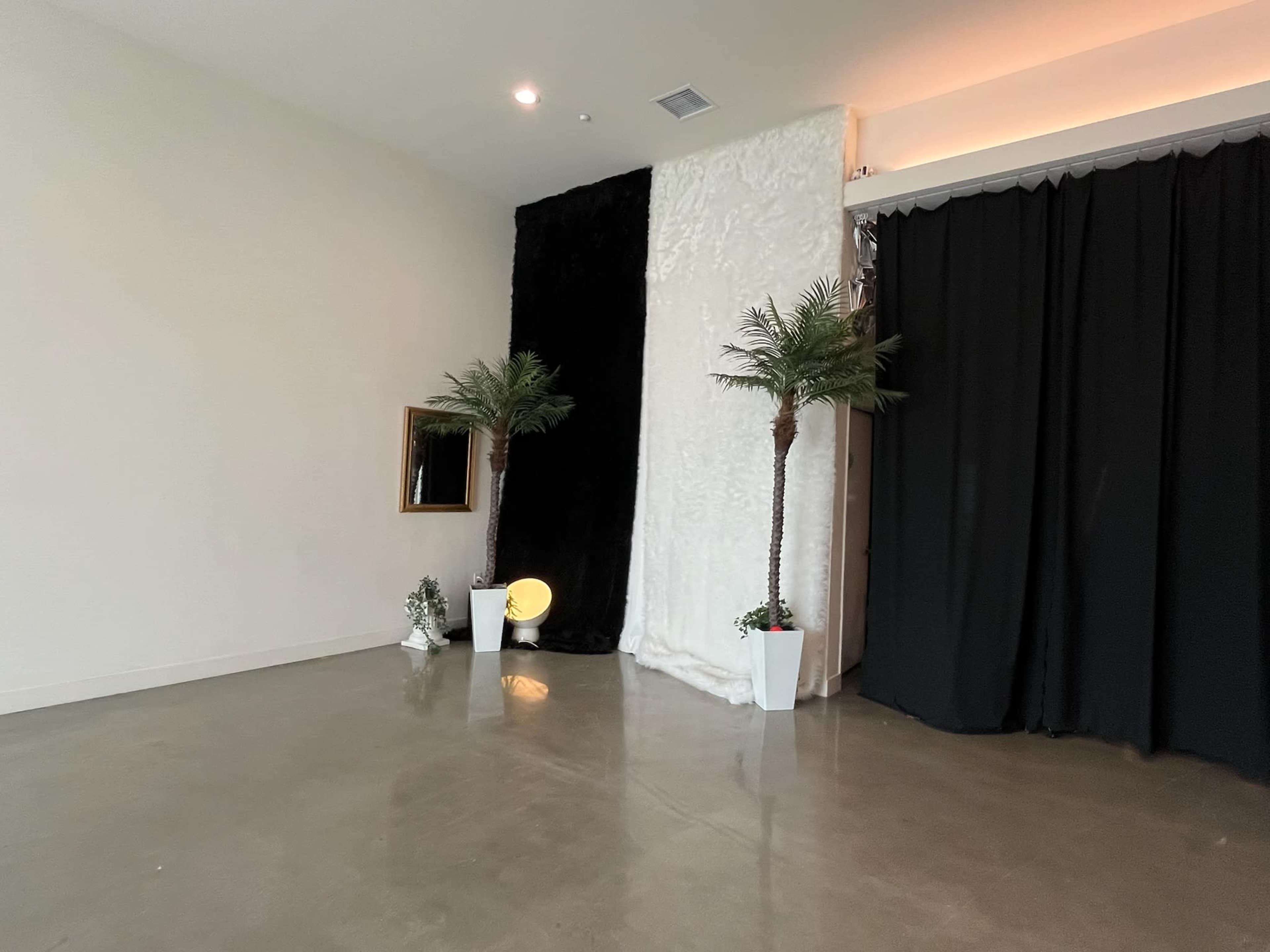 A simplified interior space featuring two tall palms in white pots, a gold-framed mirror, and a yellow chair against a backdrop of black and white fabric.