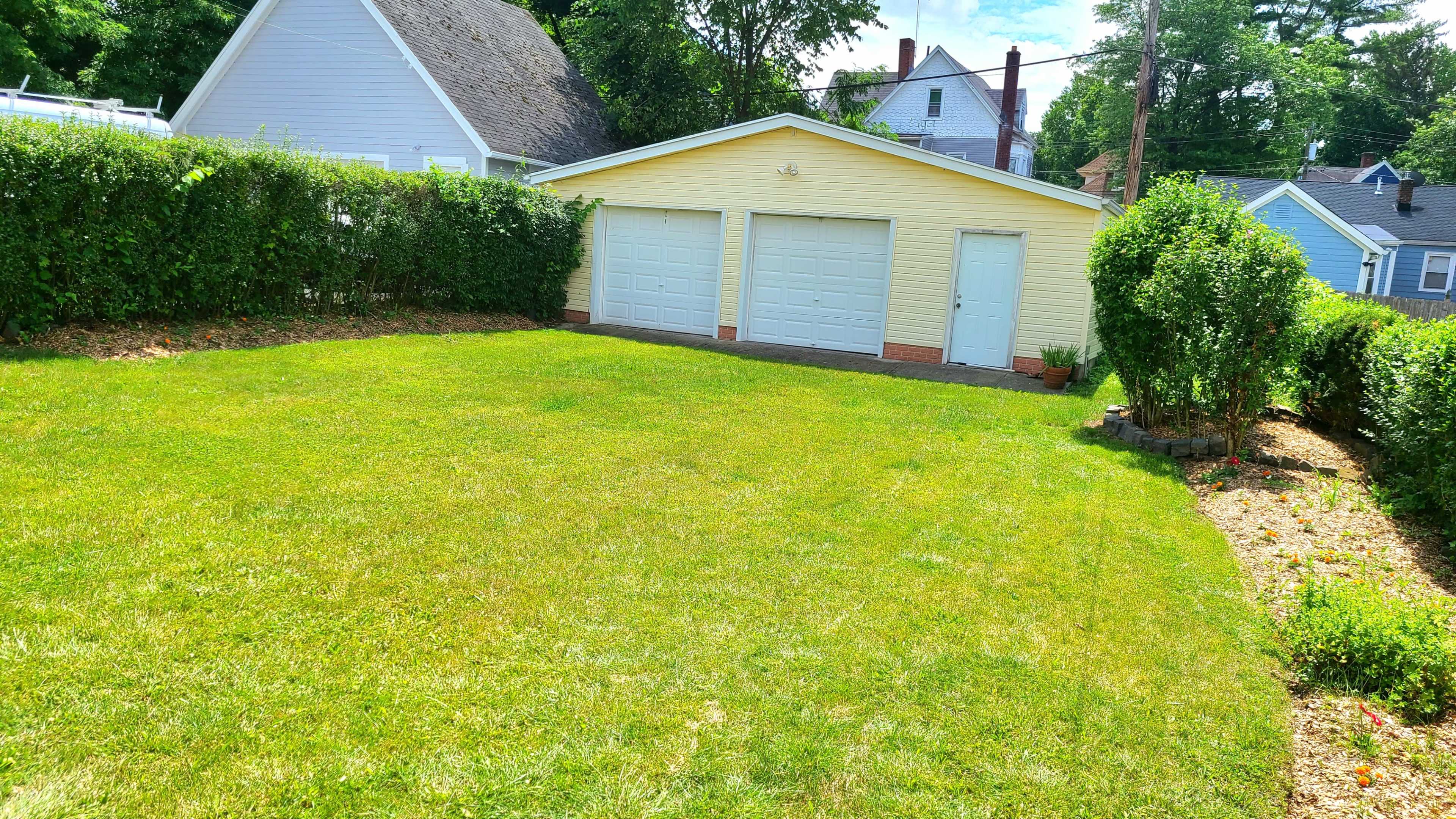A well-kept lawn with a yellow garage that has two white doors, bordered by neatly trimmed hedges.