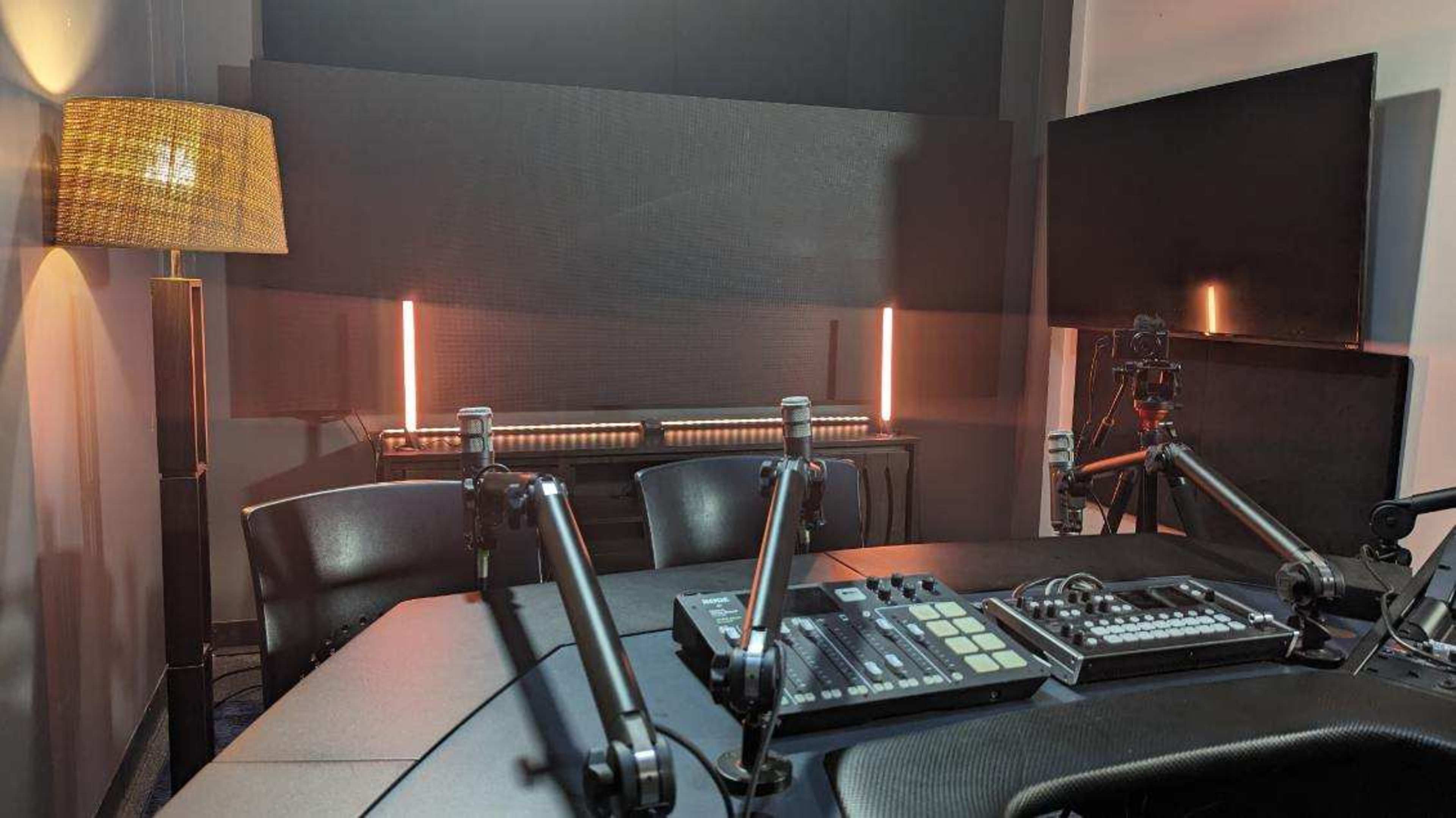 The image shows a recording studio with a circular table, microphones, and audio equipment, illuminated by soft lighting.