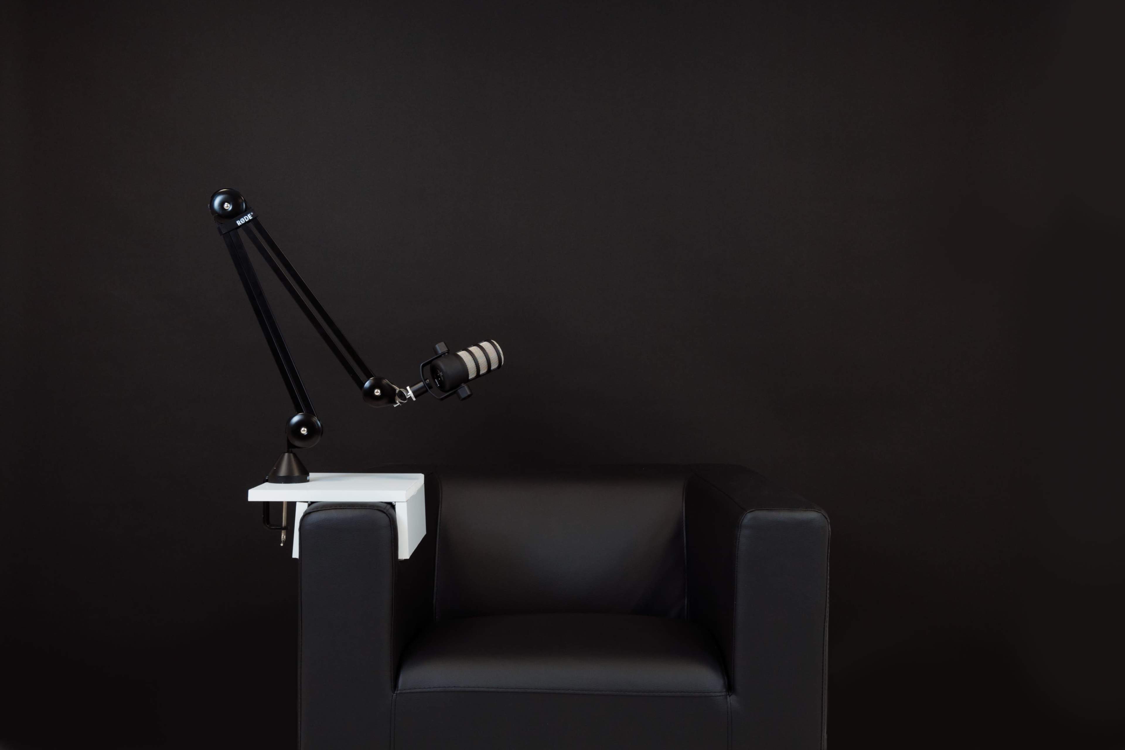 A black armchair with a microphone mounted on a white table extension is set against a dark background.