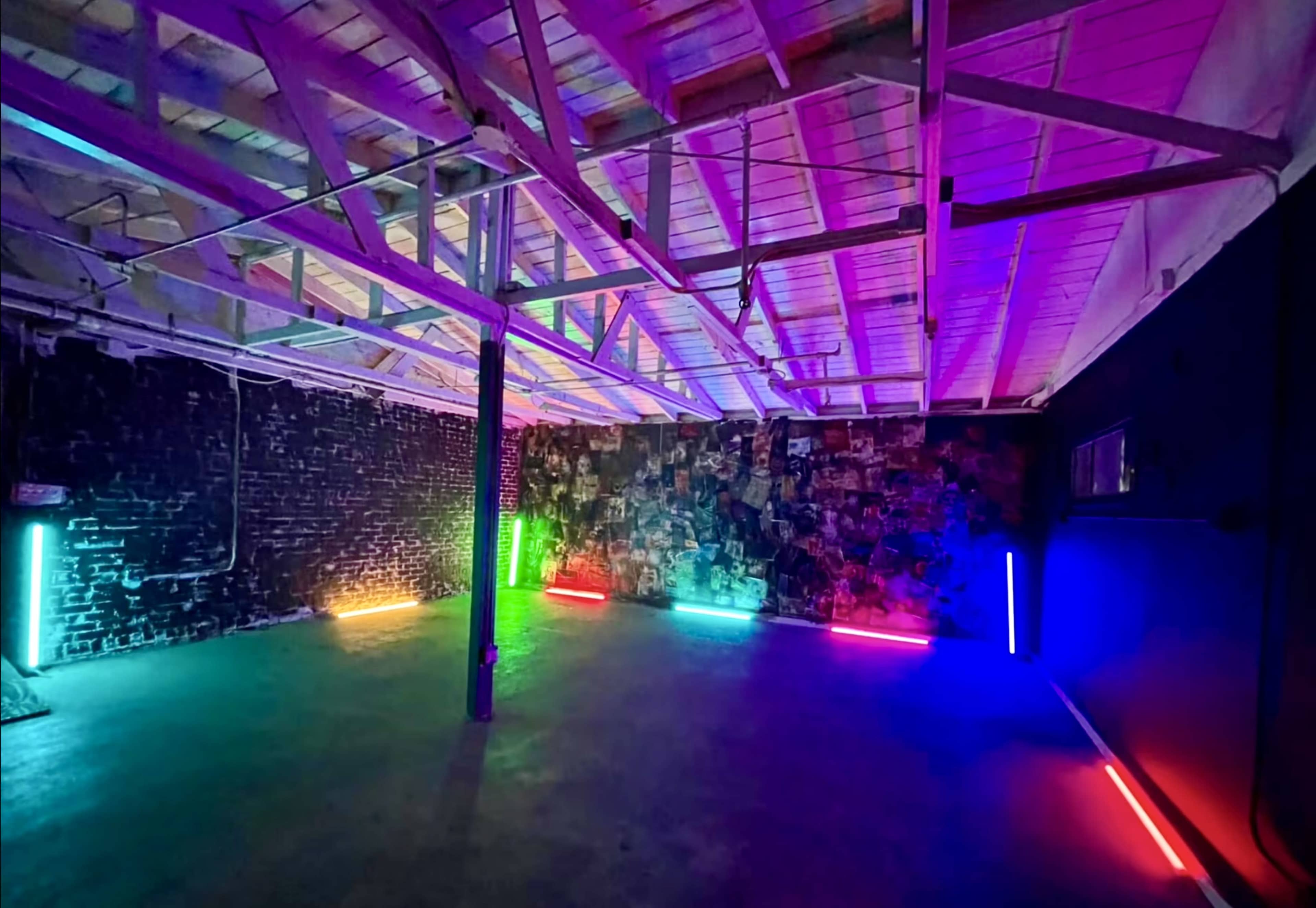 The image shows an industrial-style room with a high ceiling, featuring brightly colored neon lights along the walls.