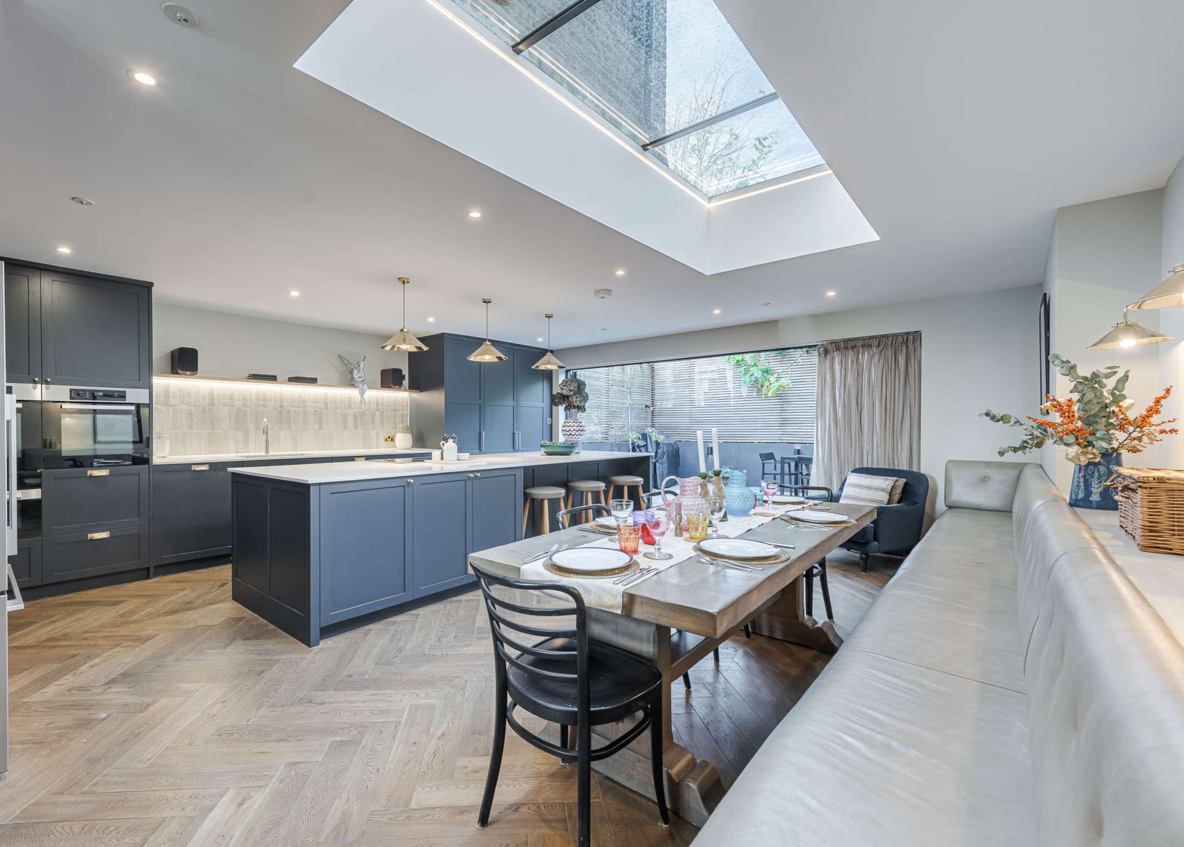 A modern kitchen features a large island with bar stools, a dining table set for a meal, and a skylight illuminating the space.