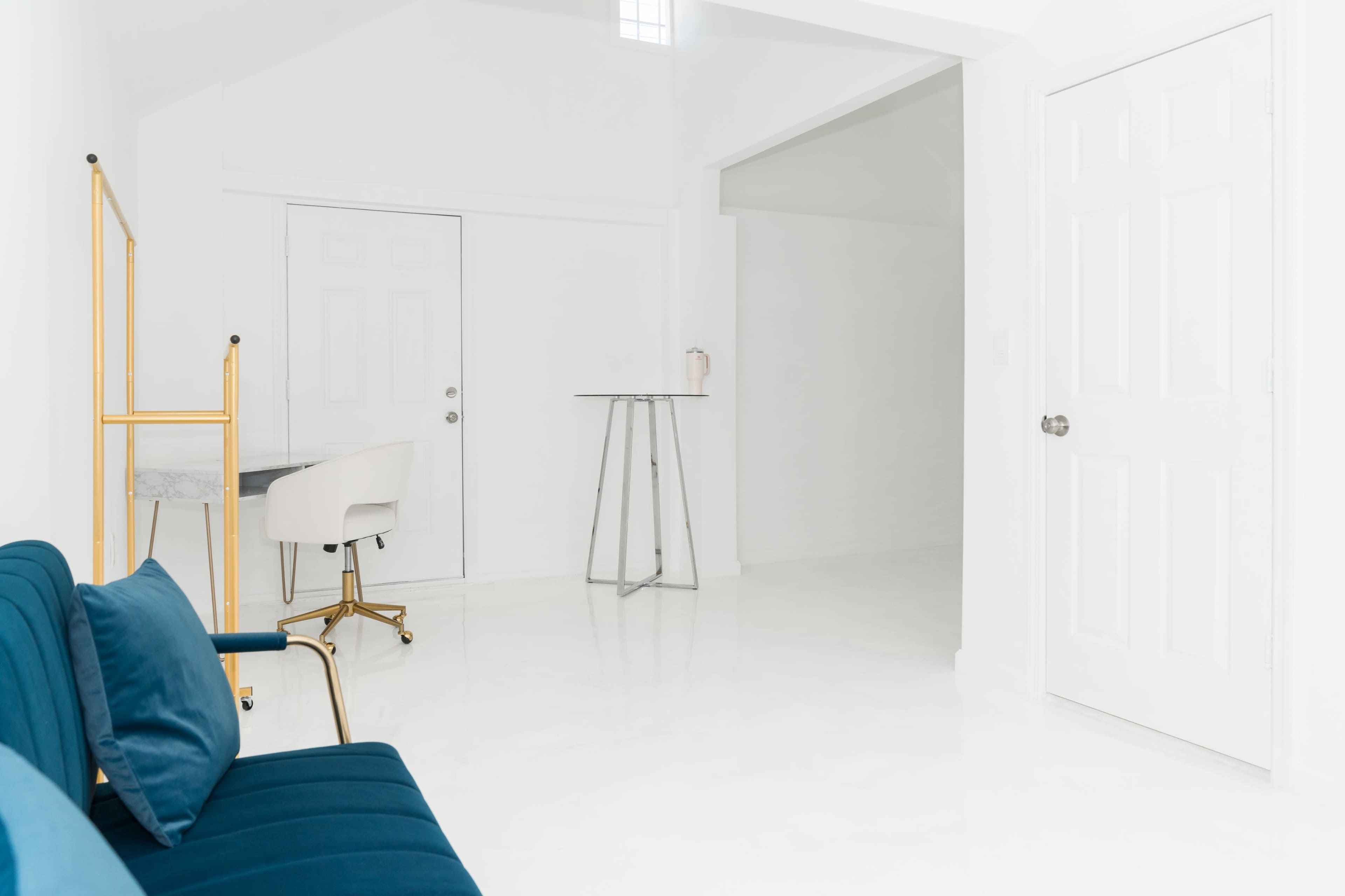 A bright, minimalist interior featuring a blue couch, a small table, and two white doors against a white wall.