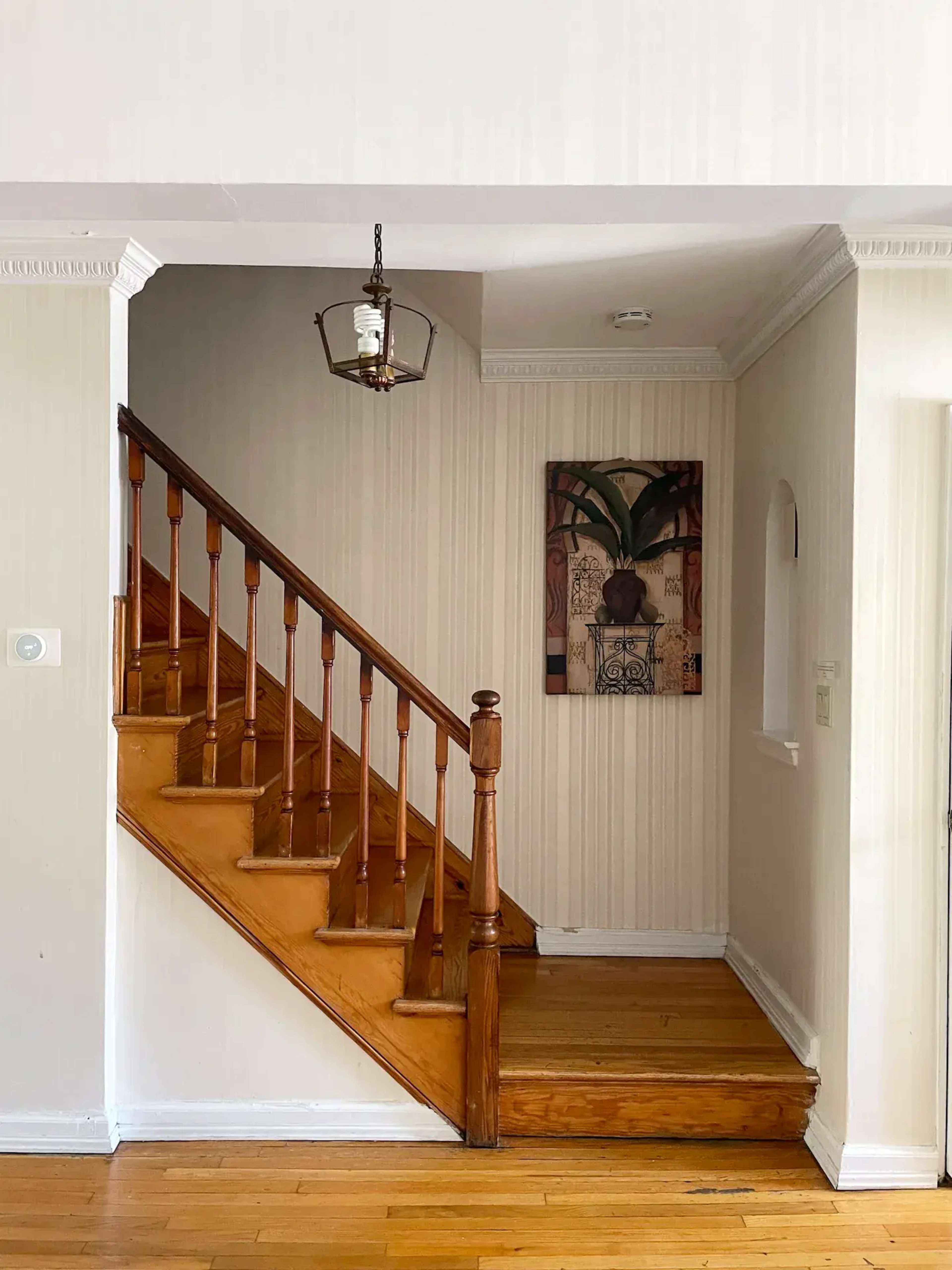 A wooden staircase leading to an upper floor, with a lantern hanging above and a framed artwork on the wall.