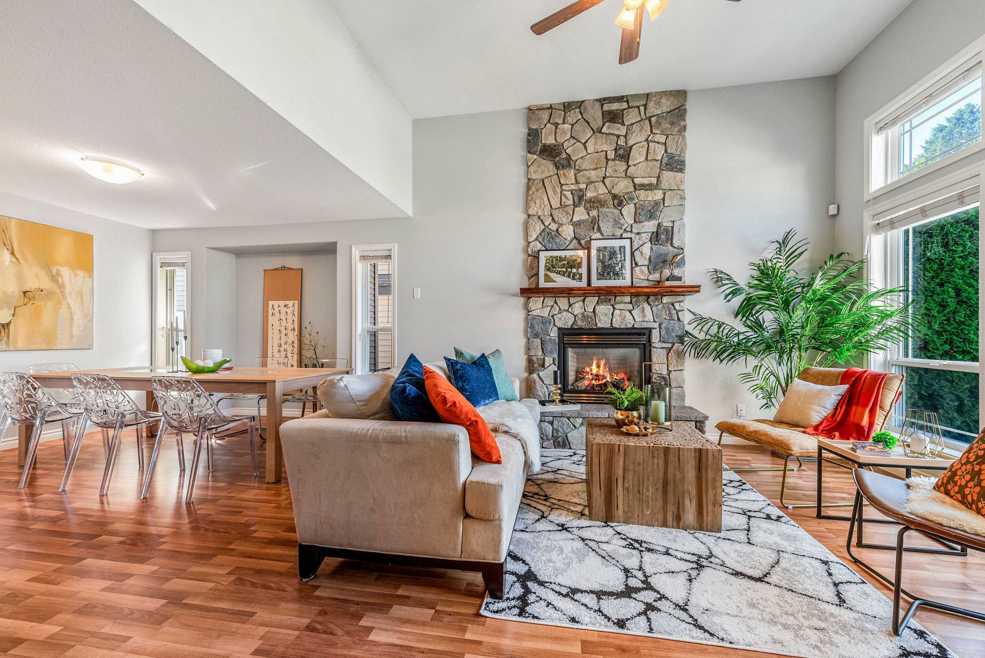 A modern living room with a stone fireplace, a wooden coffee table, and seating arranged around a large rug, adjacent to a dining area.