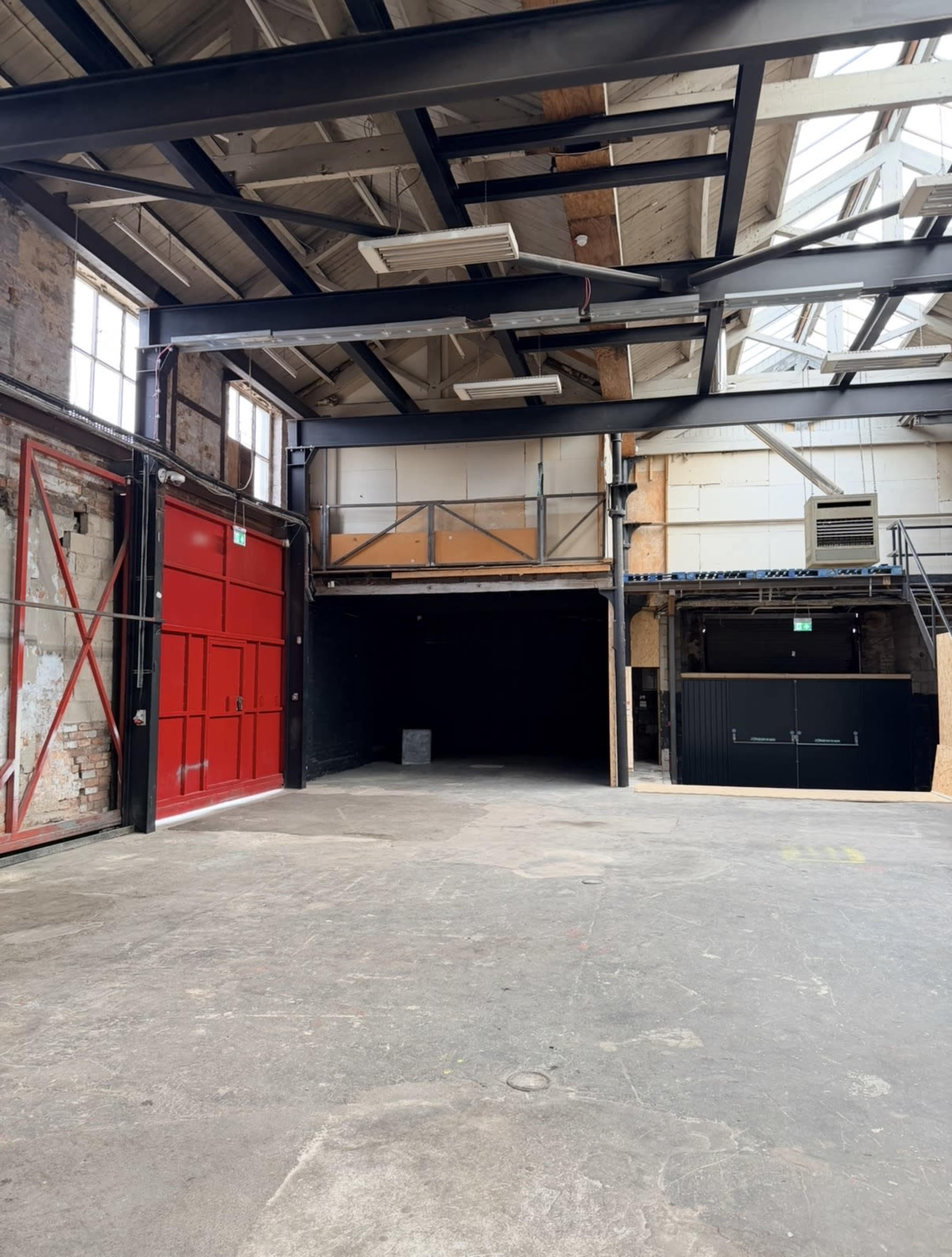 The image shows an industrial-style warehouse interior with exposed brick walls, high ceilings, and a large red door on one side.