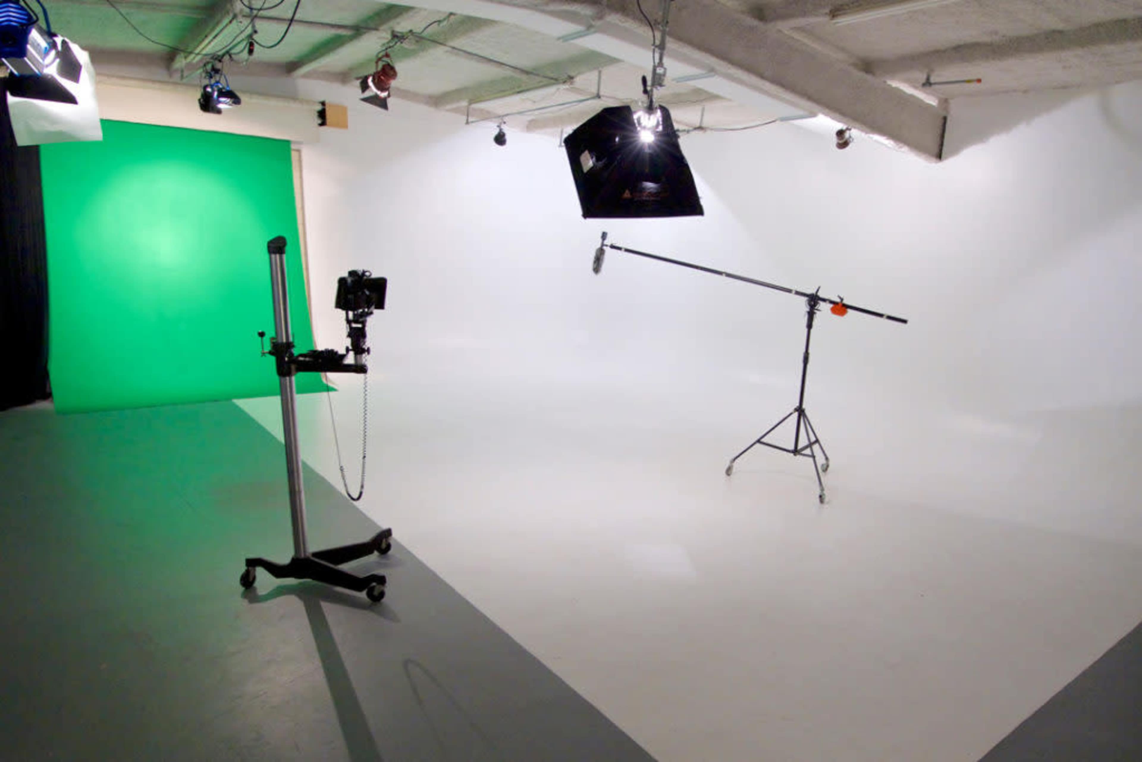A photography studio with a green backdrop, lighting equipment, and a camera on a stand.