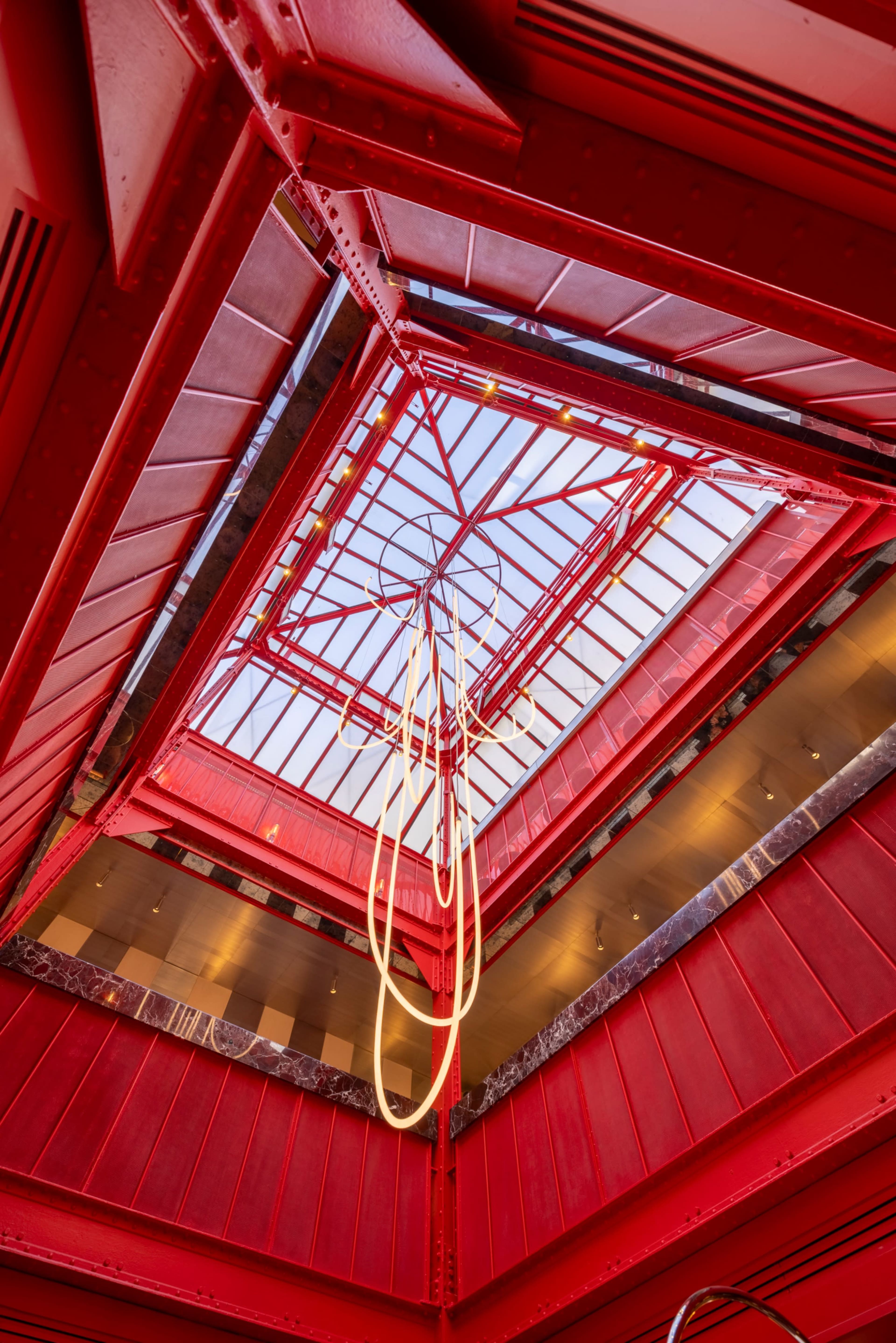 The image shows a red stairwell with geometric lines leading up to a skylight at the top.