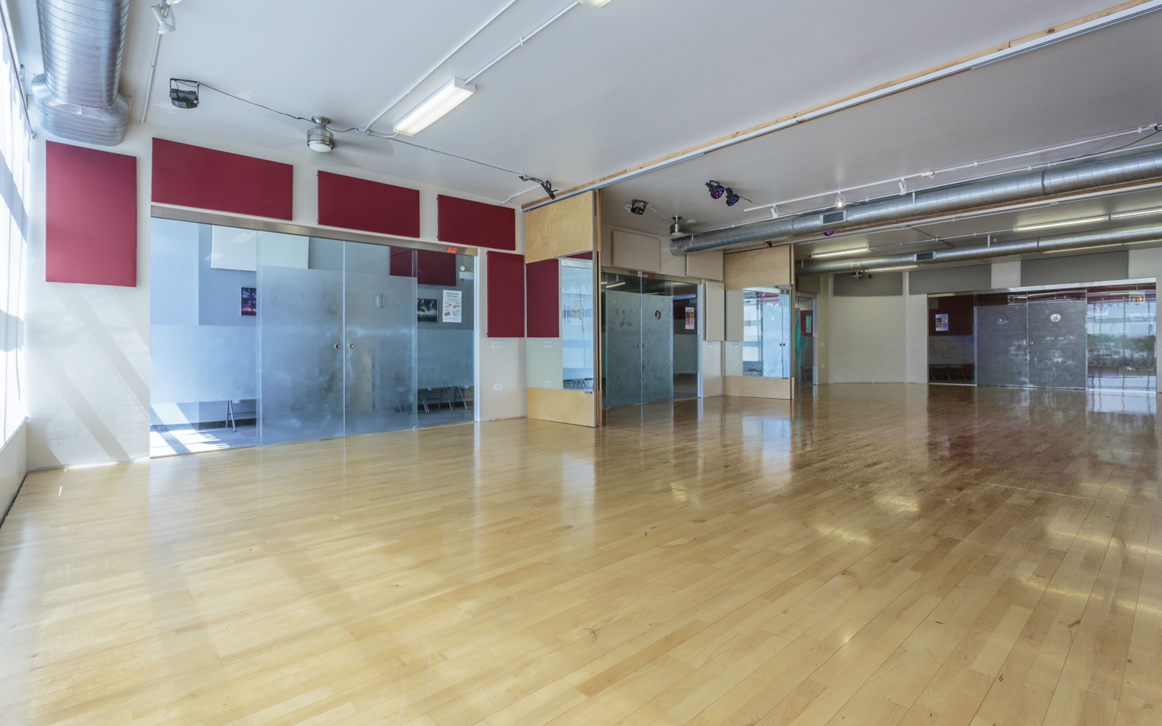 The image shows a spacious dance studio with wooden floors, large windows, and glass-walled practice rooms.