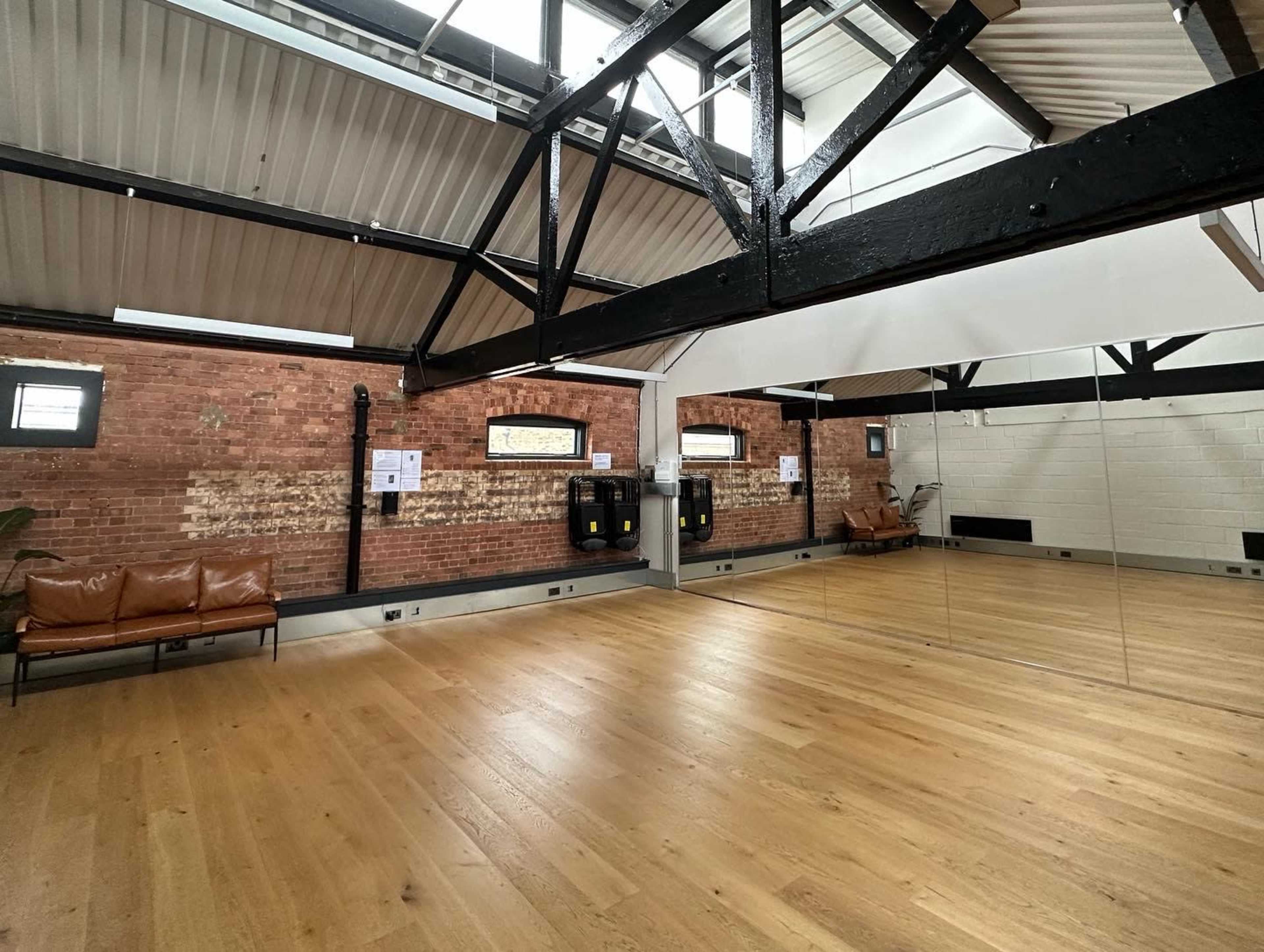A spacious interior with wooden flooring, exposed brick walls, and large mirrors along one side.