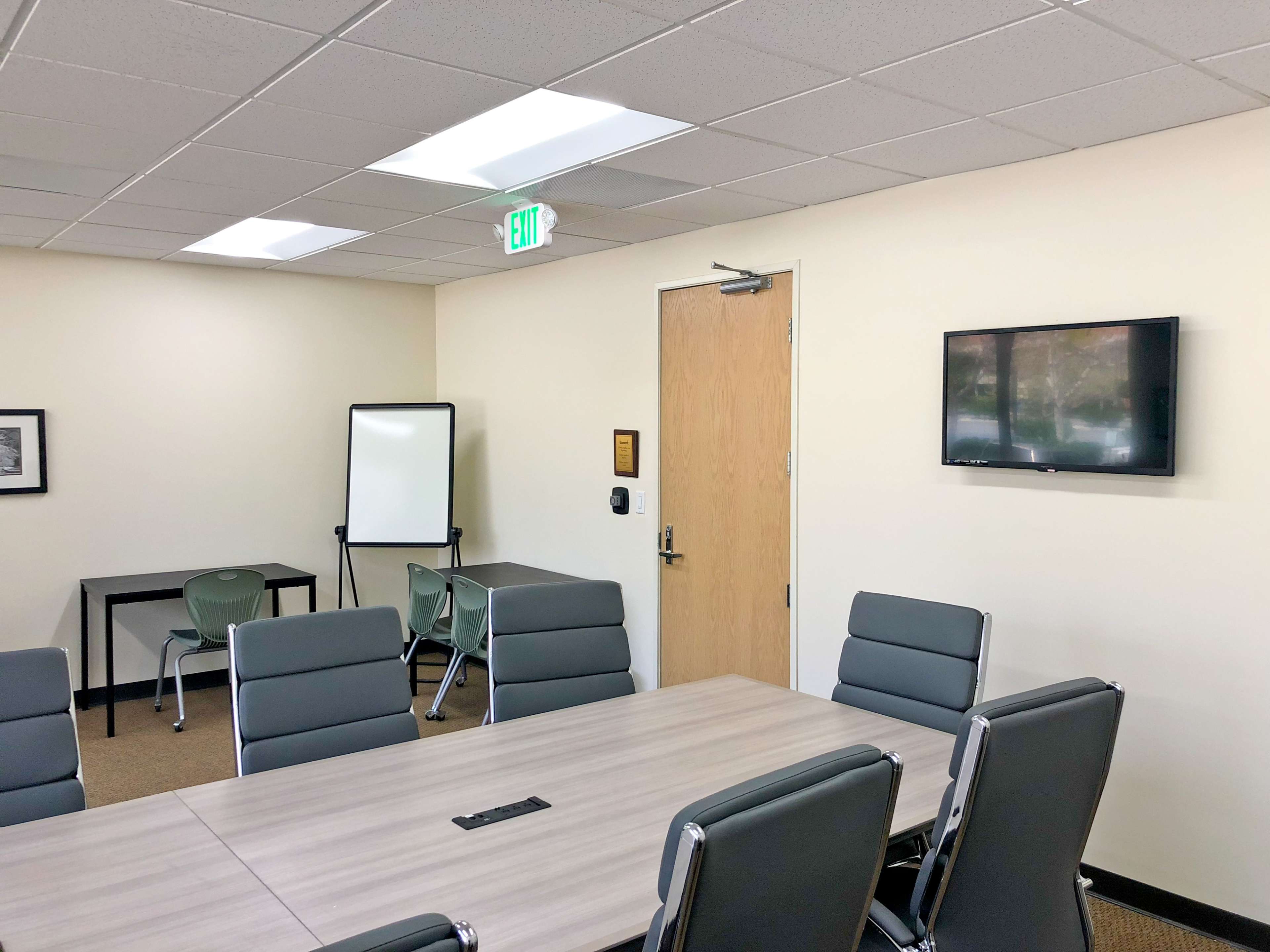 A conference room features a long table surrounded by modern chairs, a whiteboard, and a TV mounted on the wall.