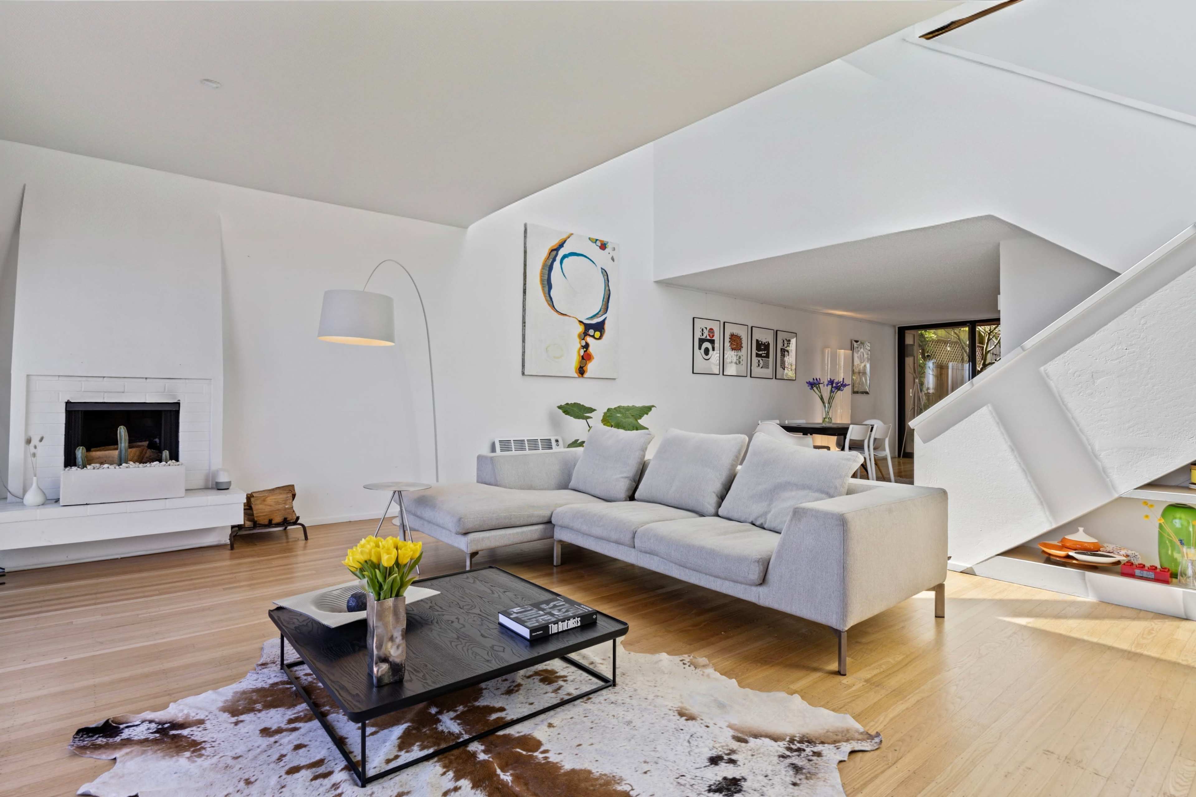 The image shows a modern living room with a light gray sofa, a black coffee table on a cowhide rug, and an adjacent dining area visible in the background.